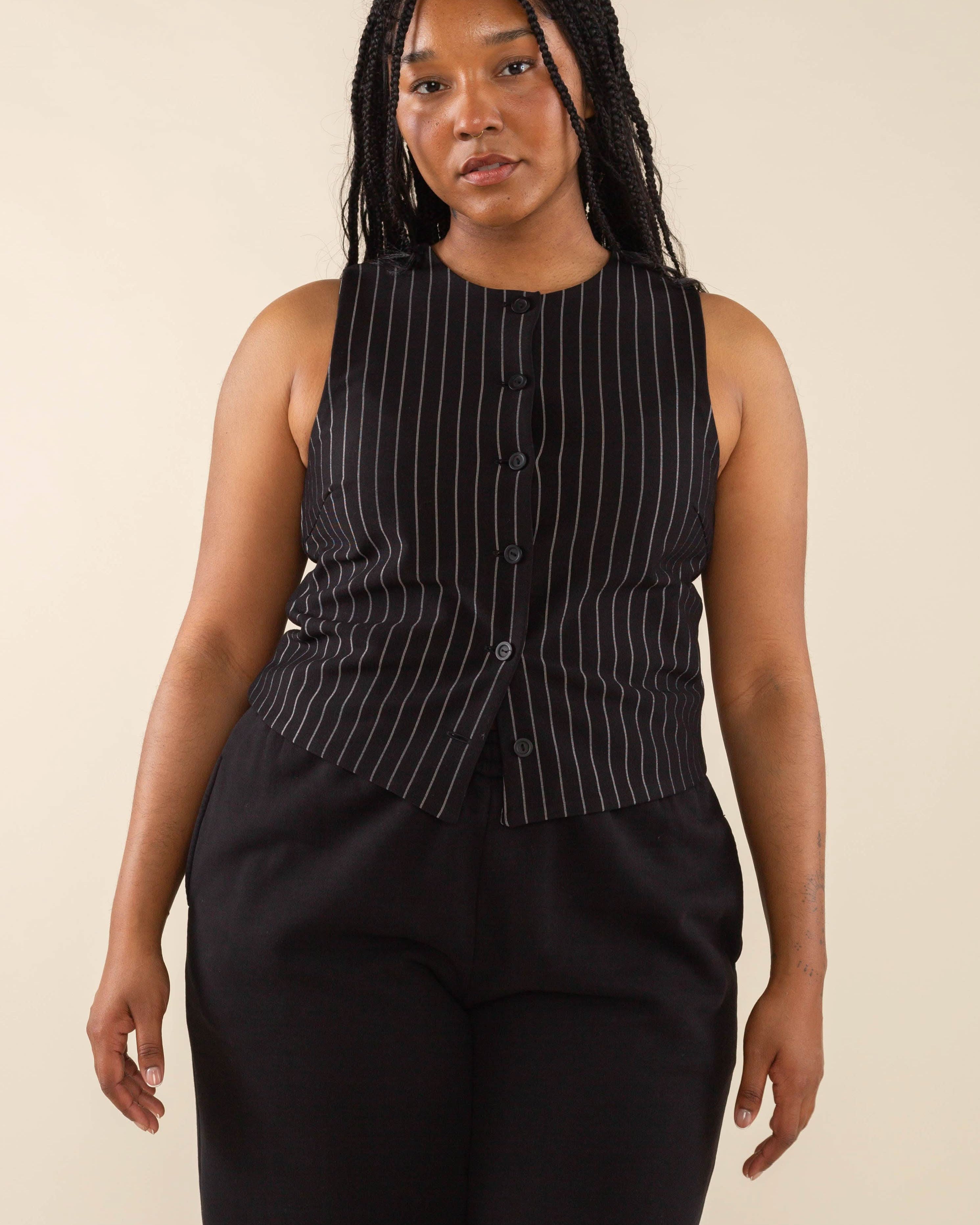 Woman wearing black high neck vest with cream pinstripes. Vest has black buttons all the way down