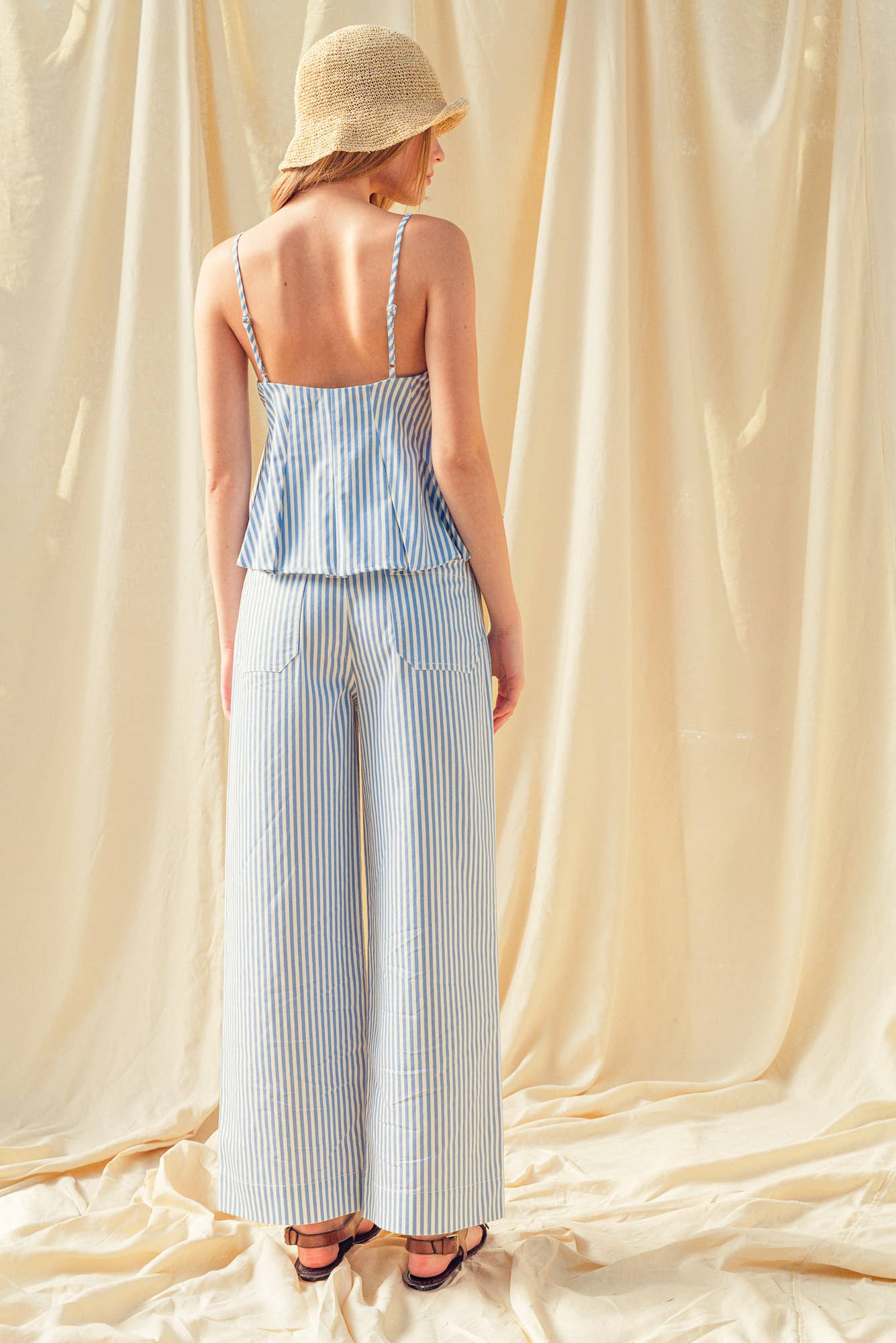 Woman wearing a striped top and wide-leg pants against a beige curtain backdrop