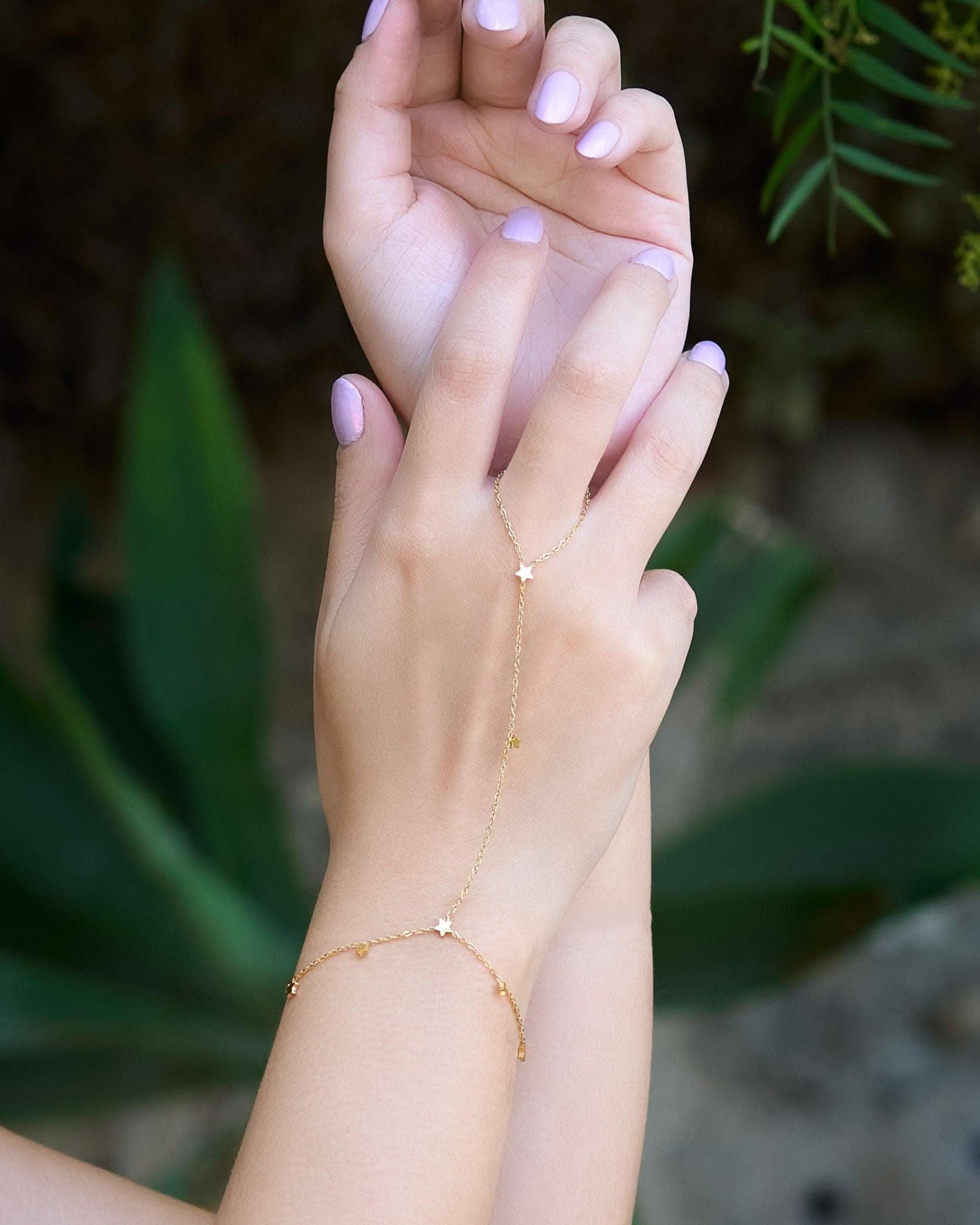 Hand wearing a delicate gold hand chain bracelet connected to a thin ring