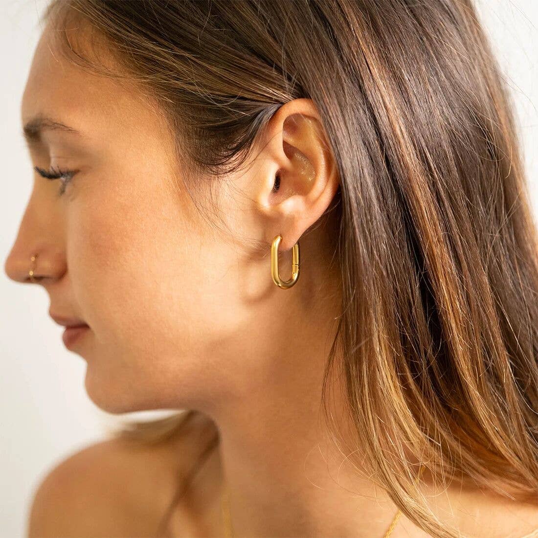 Close-up of a woman wearing a gold hoop earring against a neutral background