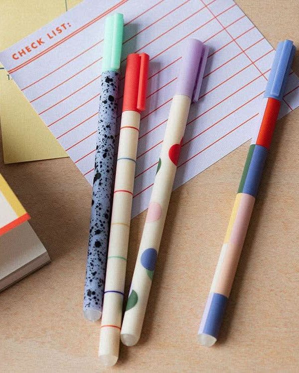 Four colorful pens laying on top of sticky notes on desk