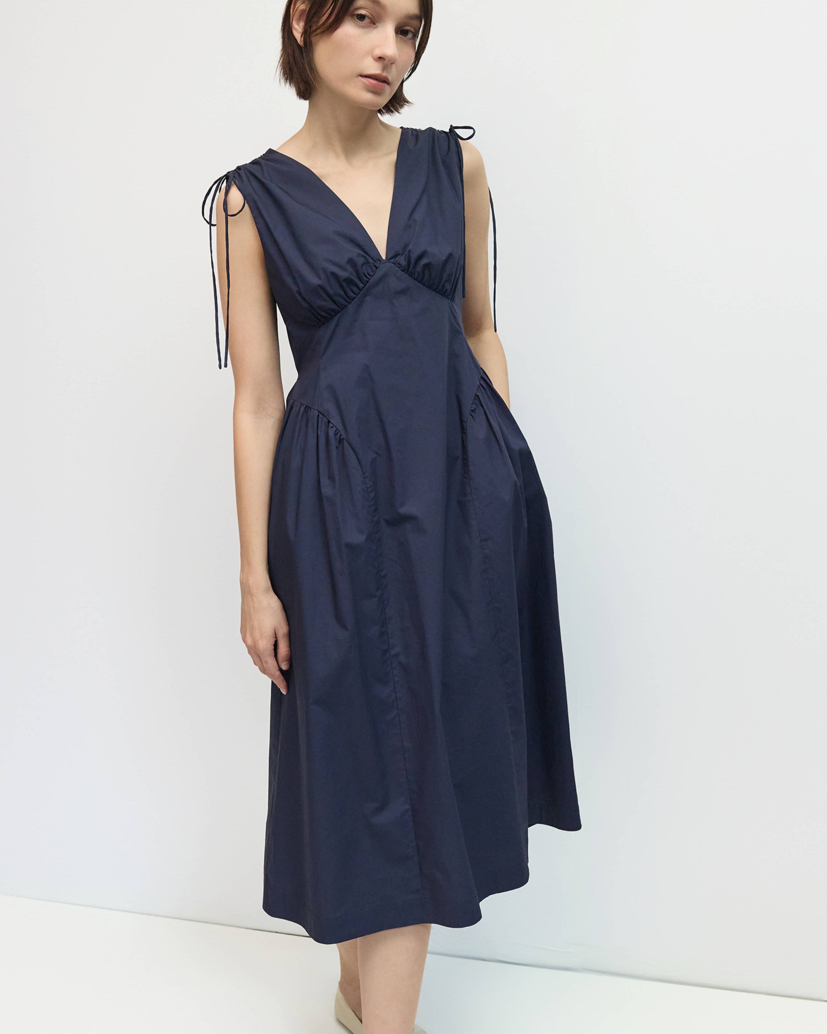Woman wearing a navy blue dress with ribbon straps against a white background