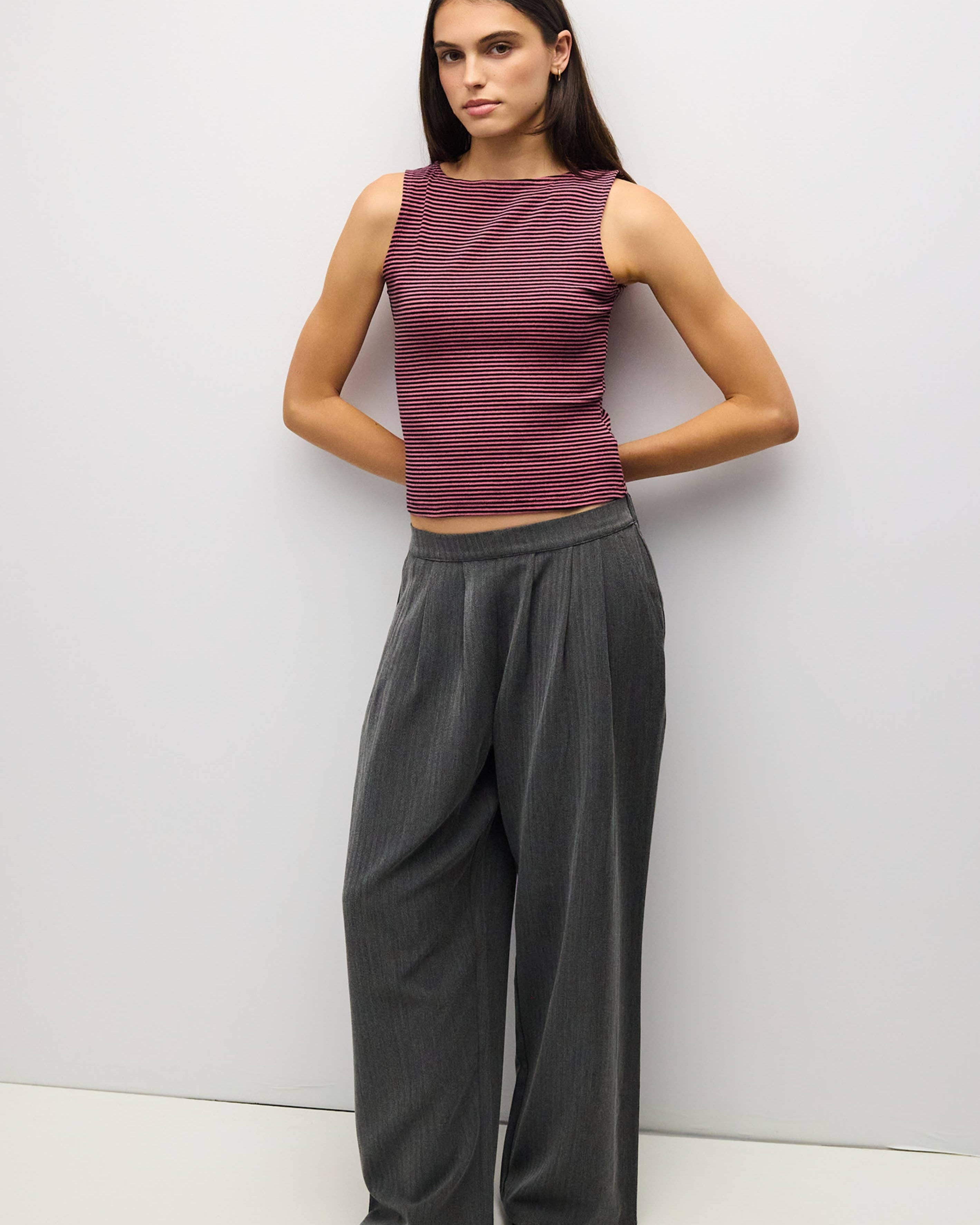 A woman modeling a sleeveless ribbed knit top in heathered burgundy and wide-leg pleated trousers in dark gray, standing against a plain light gray studio wall.