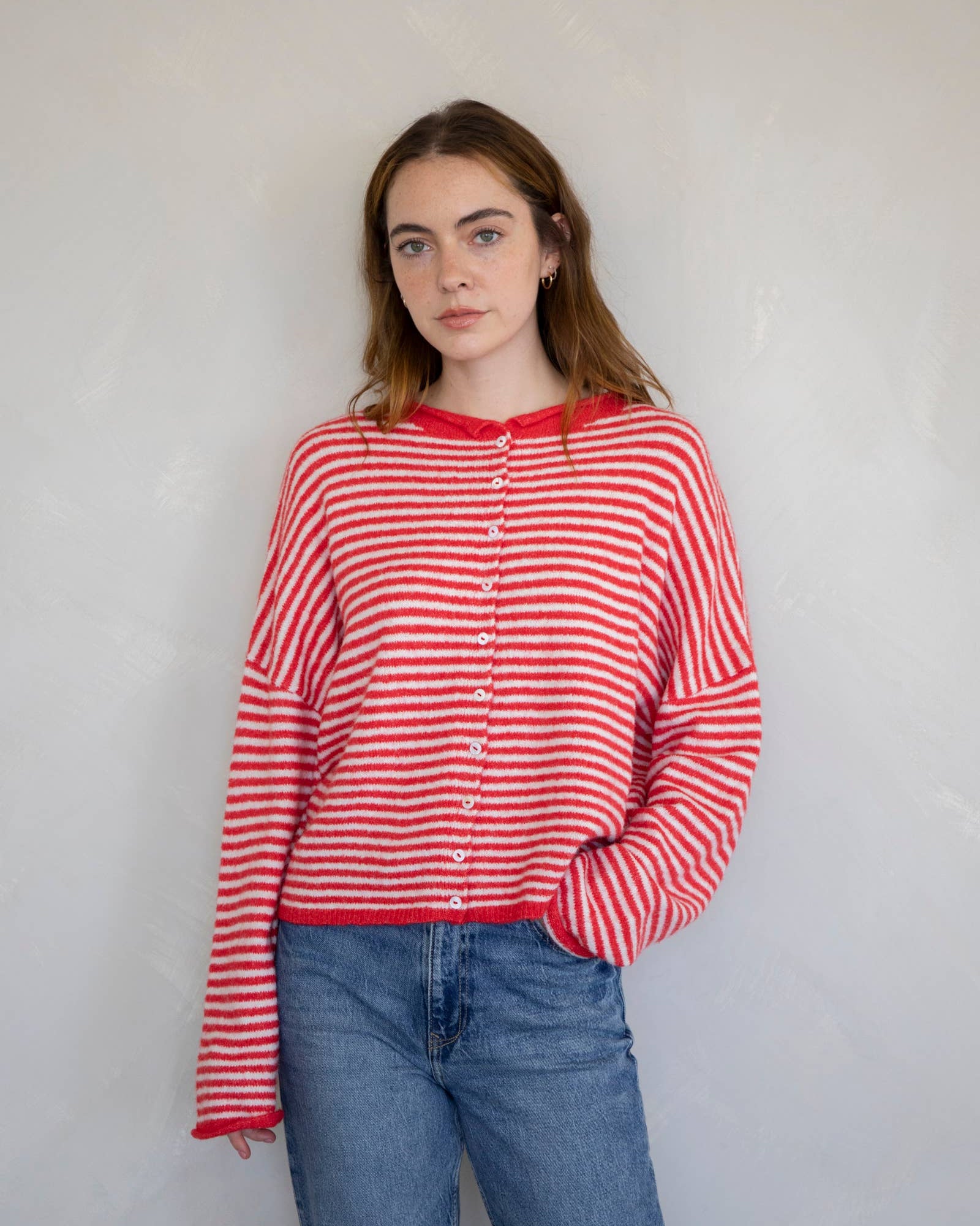 Woman wearing a red and white striped shirt and blue jeans against a plain background