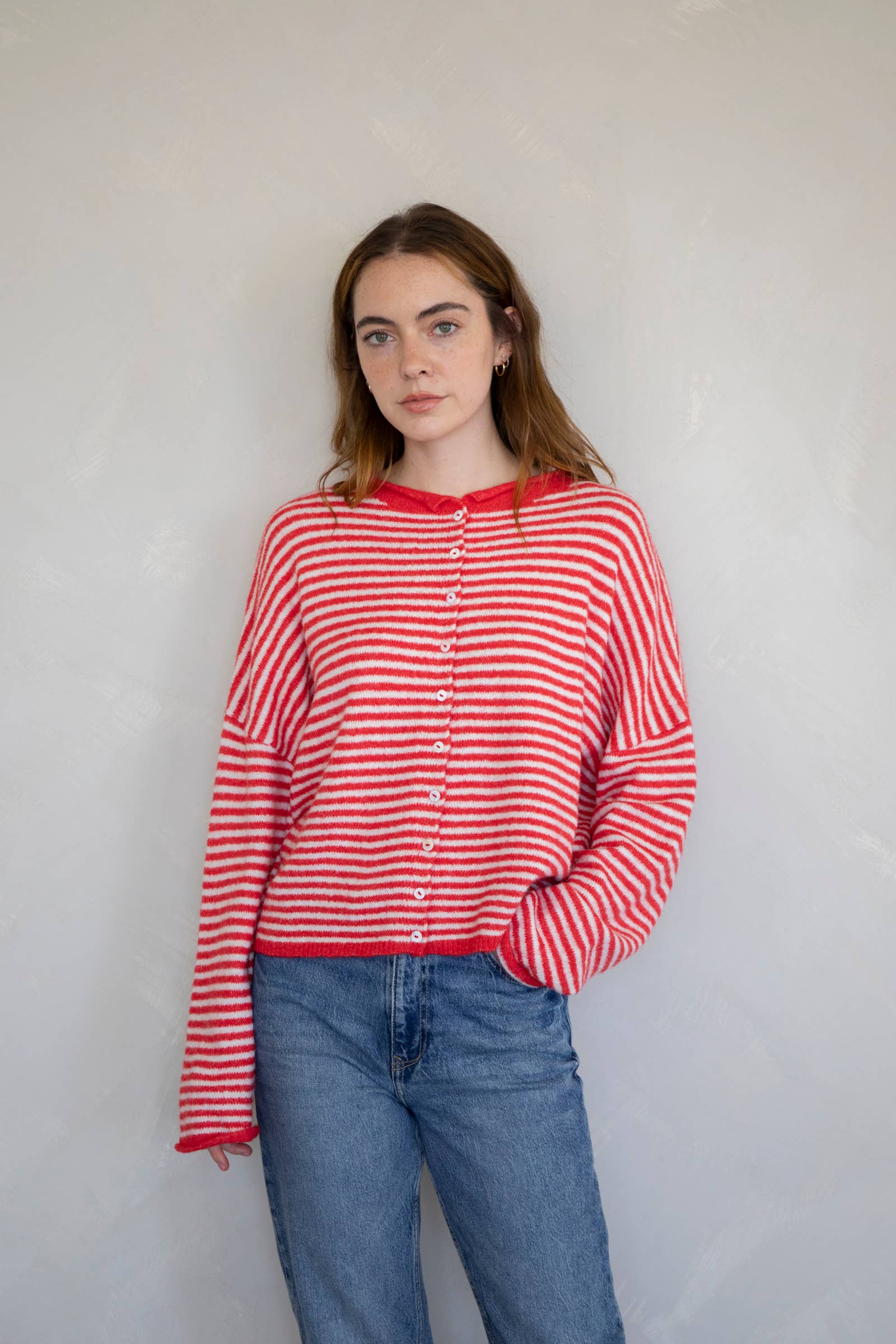 Woman wearing a red and white striped shirt and blue jeans against a plain background