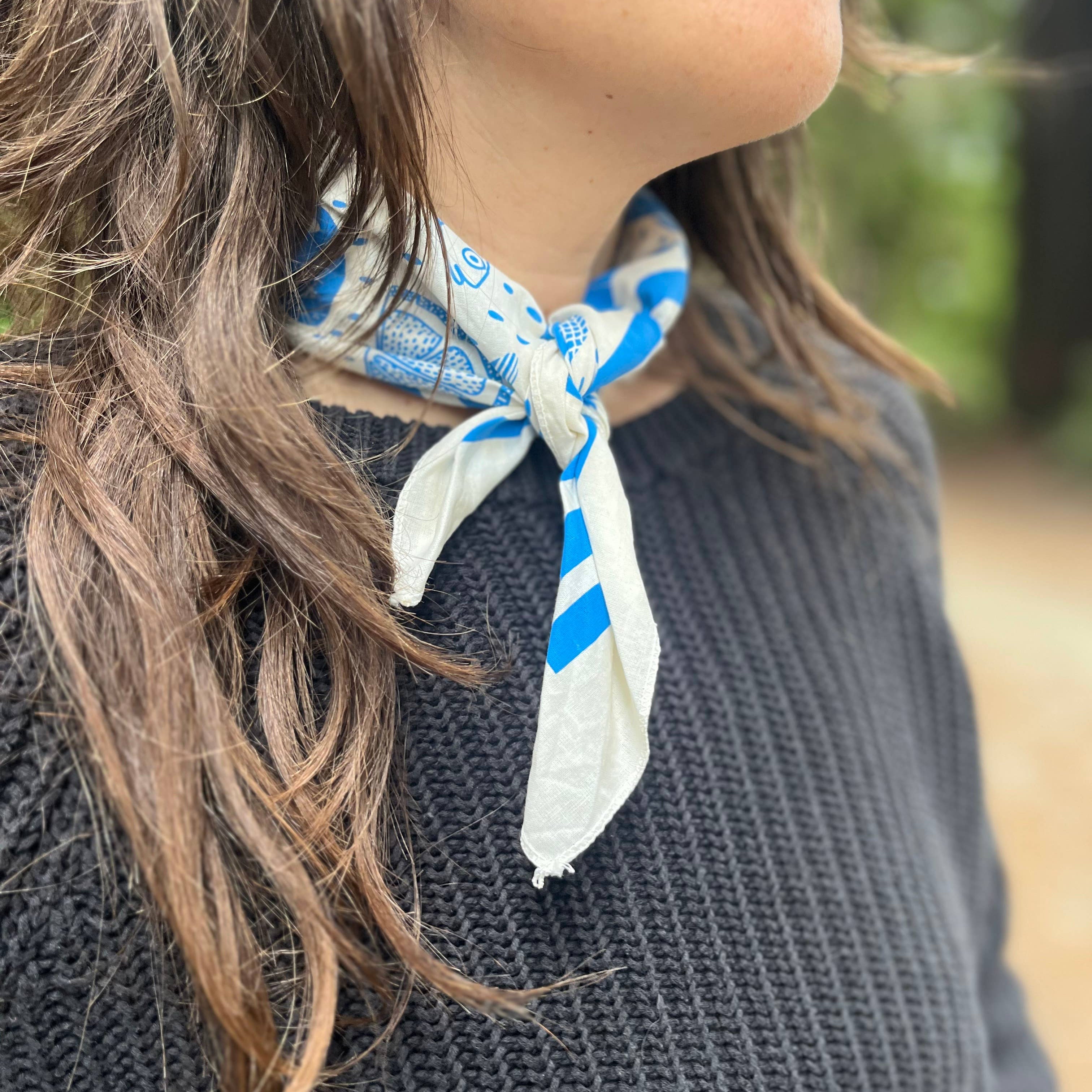 Person wearing a blue and white patterned scarf around their neck with a blurred natural background