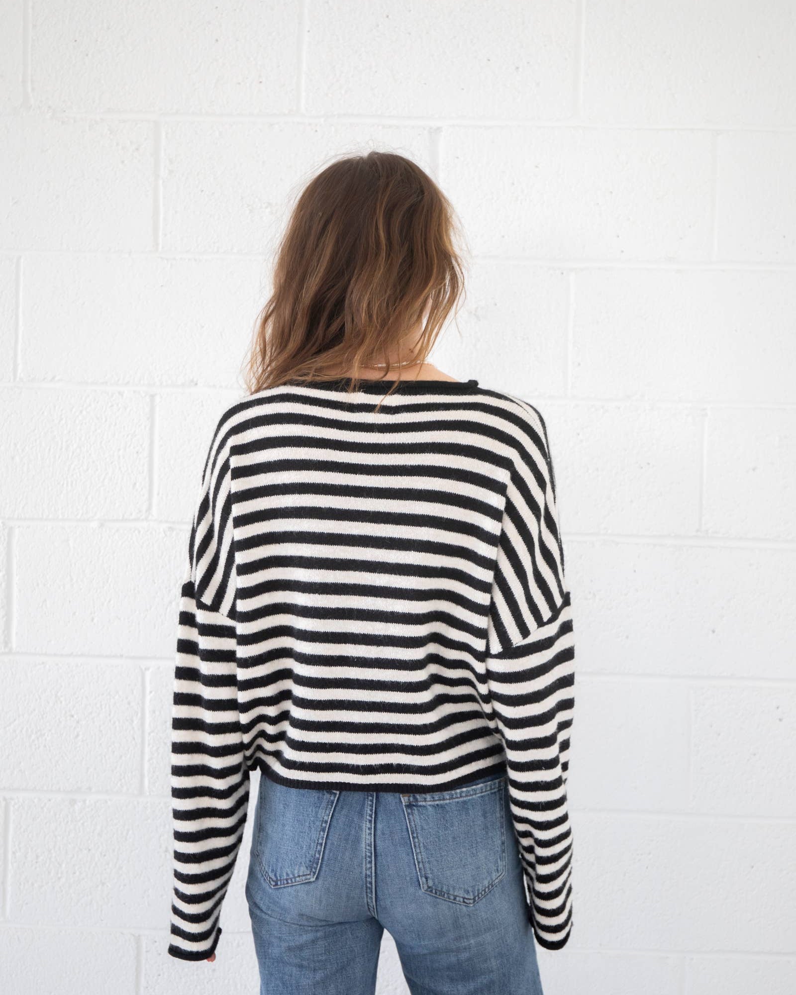 Person wearing a black and white striped sweater and blue jeans against a white wall.