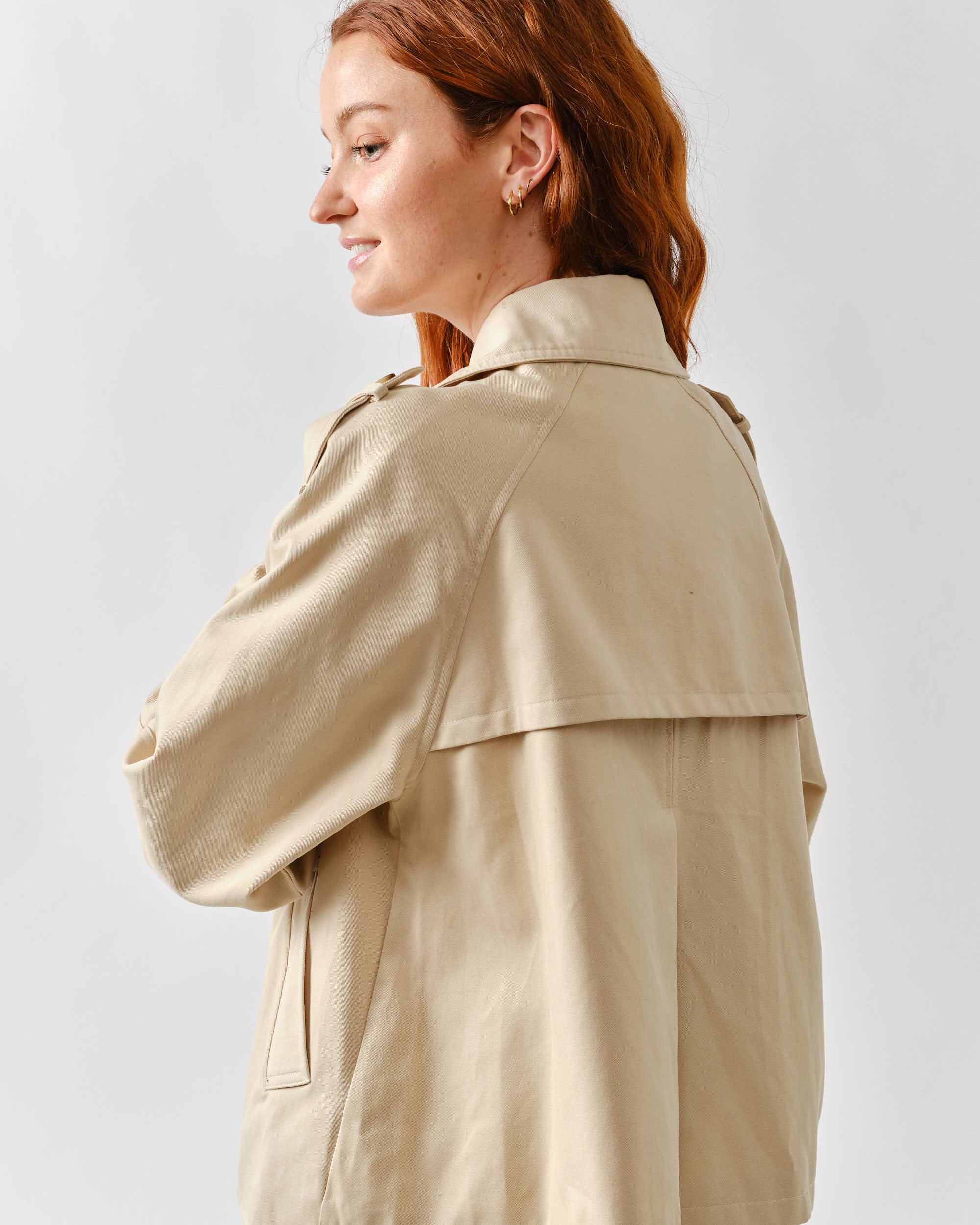 Woman wearing a beige trench coat against a white background
