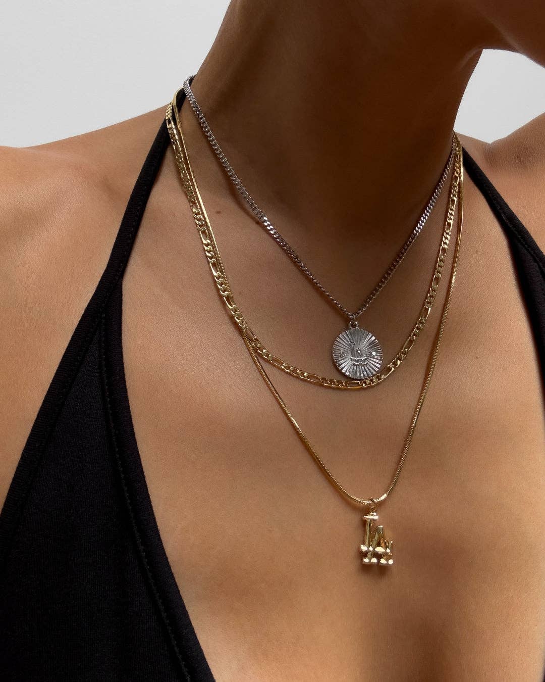 Layered gold necklaces on a person wearing a black top against a neutral background