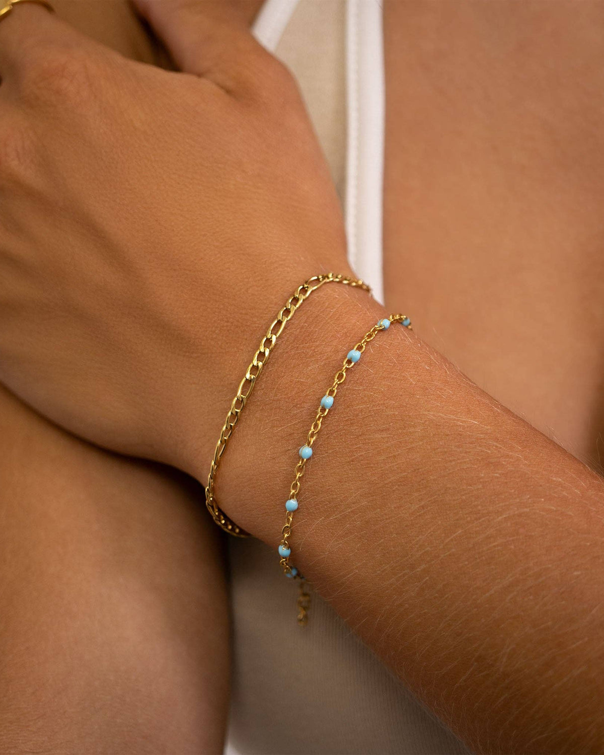 Close-up of a wrist wearing two gold bracelets with turquoise beads on a neutral background