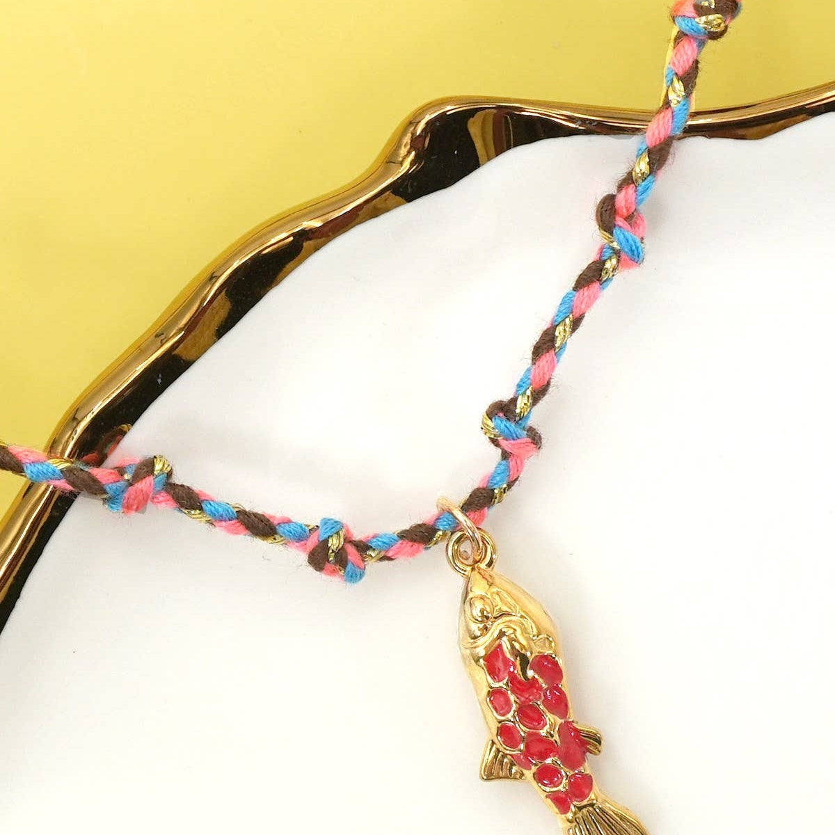Necklace with a fish charm on a white surface with a gold leaf background