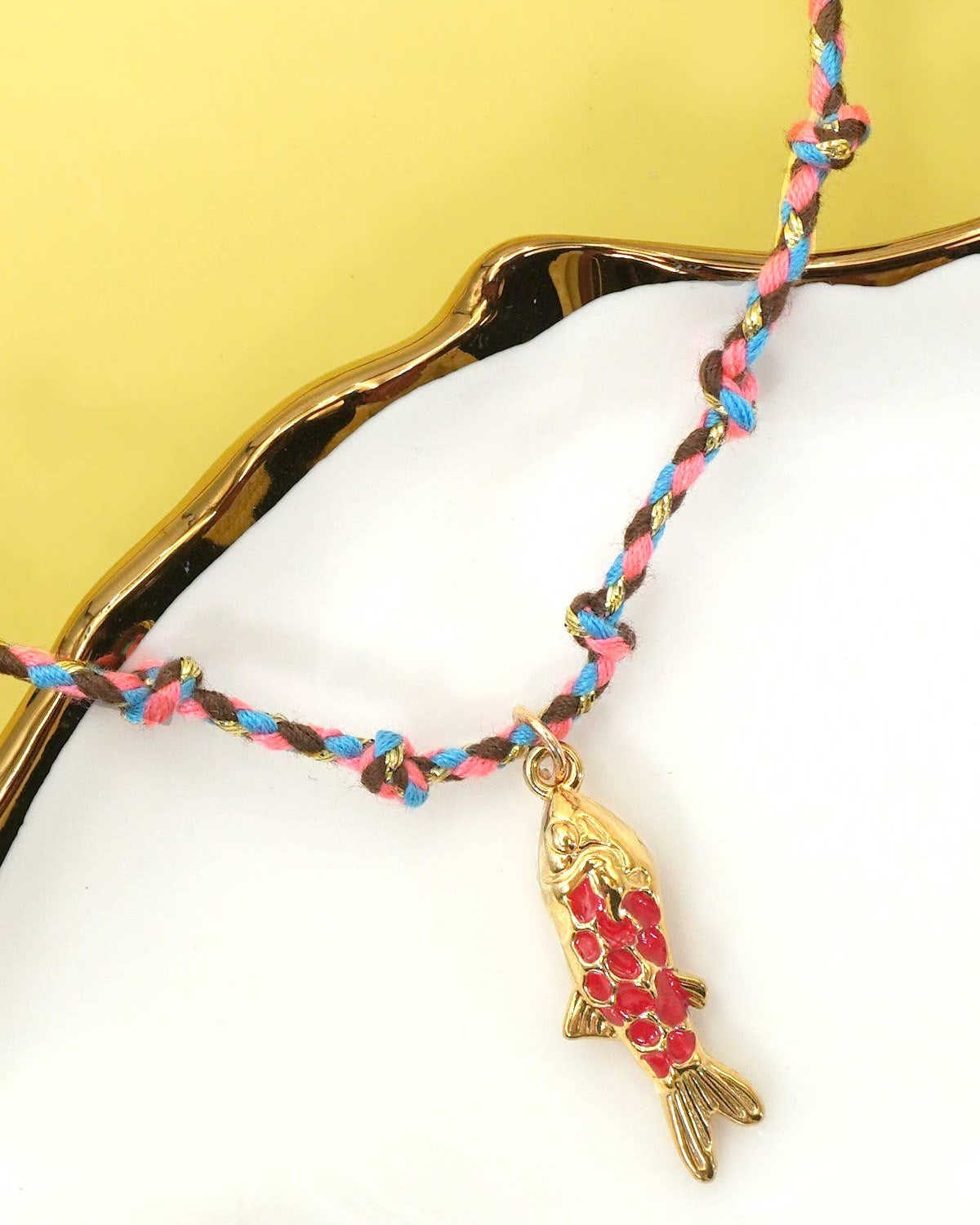 Necklace with a fish charm on a white surface with a gold leaf background