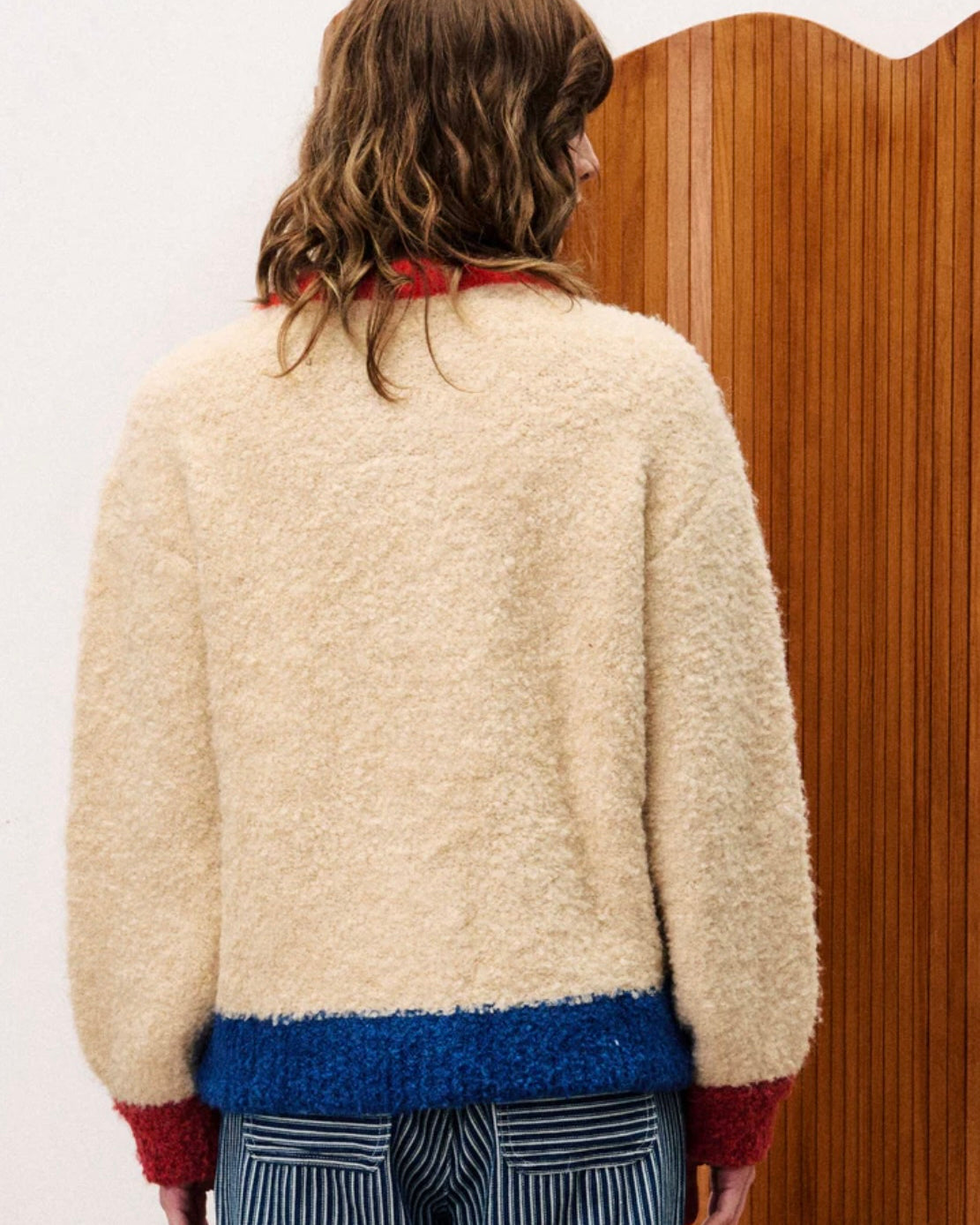 Person wearing a cream sweater with red cuffs and blue hem