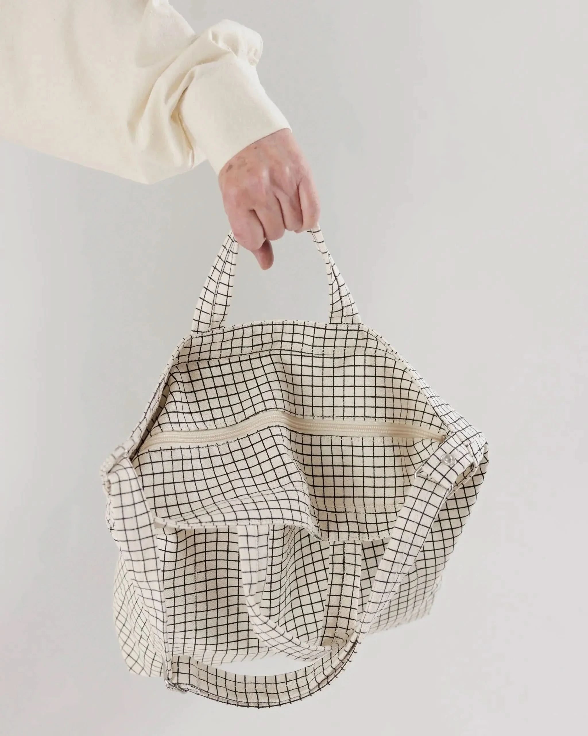 Shot of BAGGU zipper details on white background. BAGGU bag is a square tote bag with adjustable strap with white with black grid line design