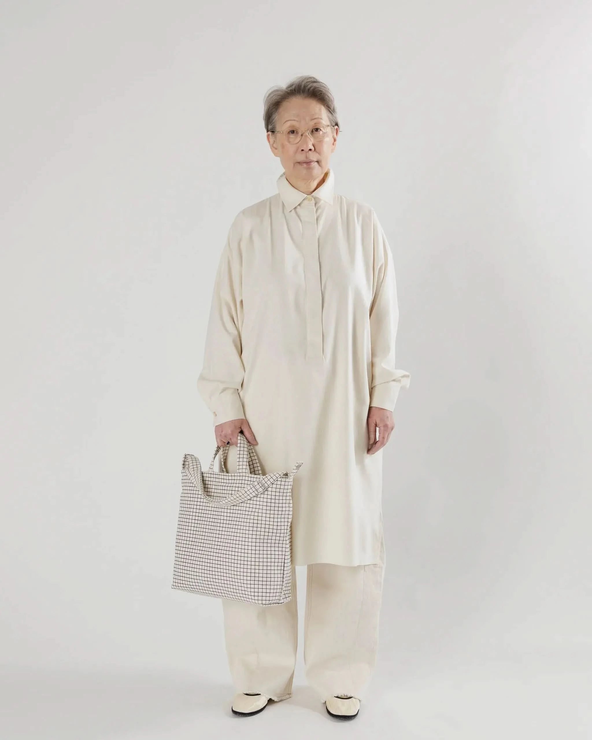 Model wearing cream set on white background holding BAGGU bag is a square tote bag with adjustable strap with white with black grid line design