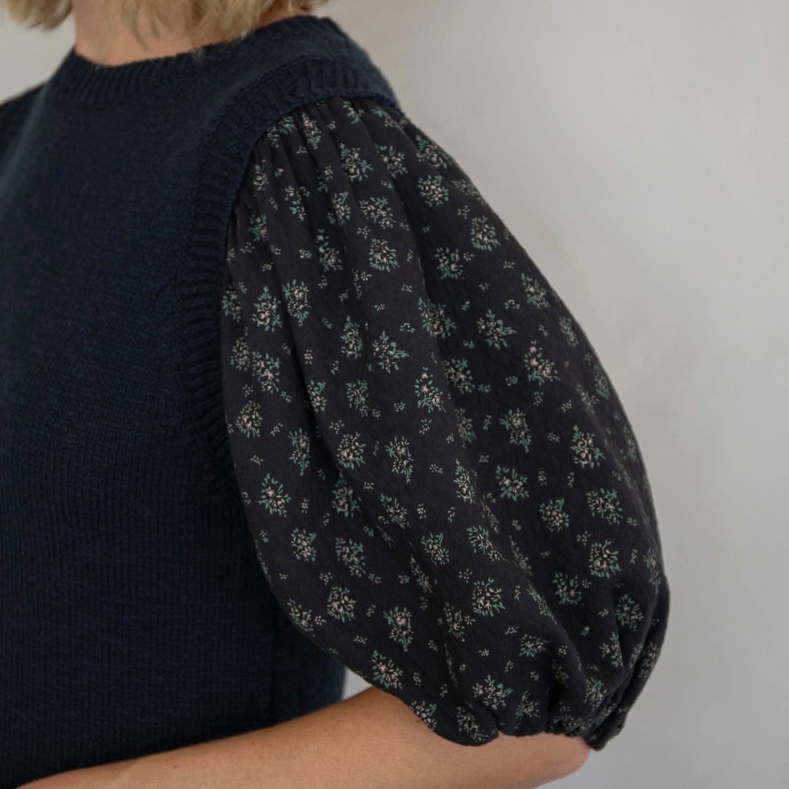Person wearing a dark blue sleeveless top with floral patterned sleeves against a plain background