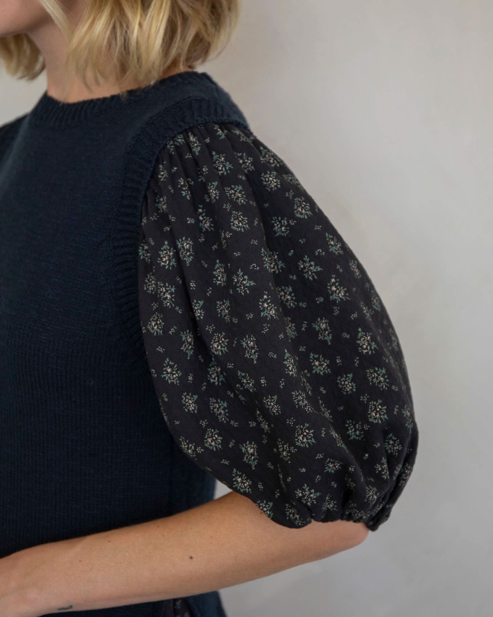 Person wearing a dark blue sleeveless top with floral patterned sleeves against a plain background