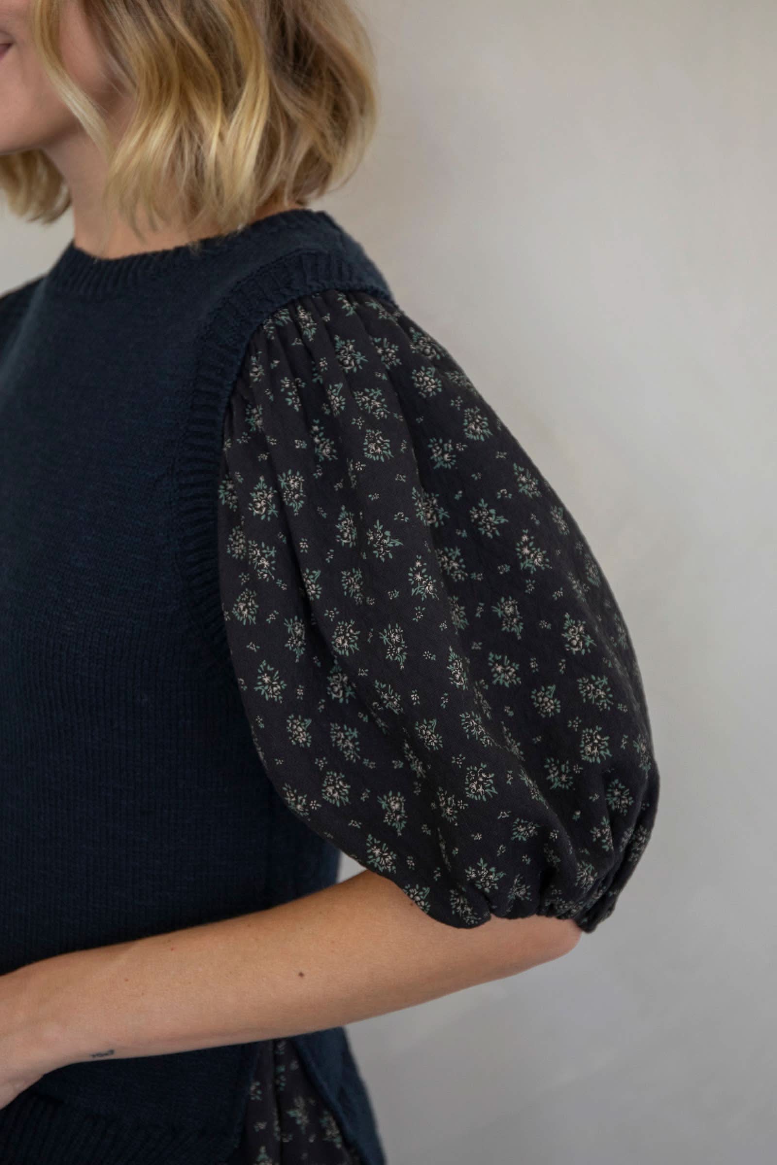 Person wearing a dark blue sleeveless top with floral patterned sleeves against a plain background