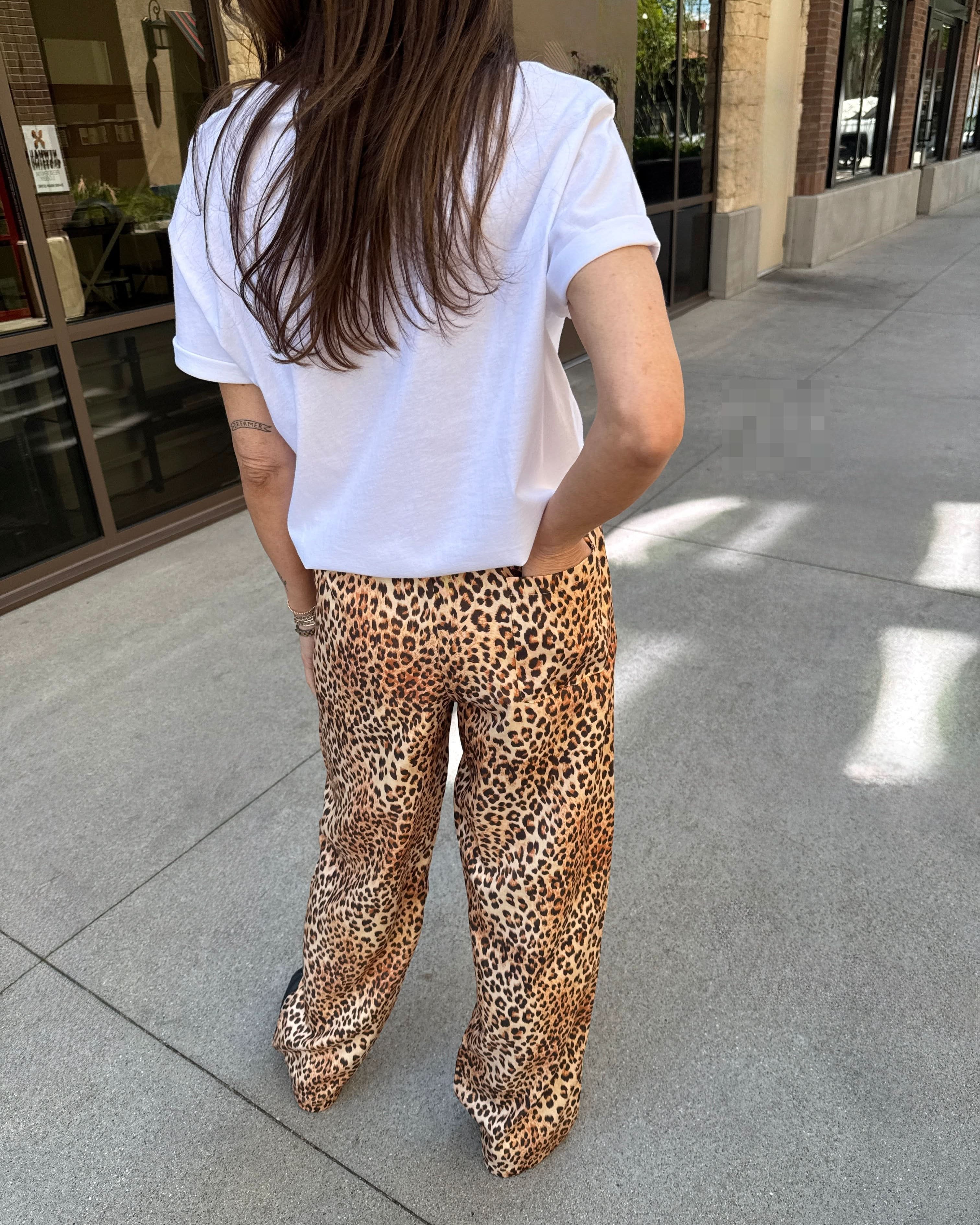 Person wearing a white t-shirt and leopard print pants standing on a sidewalk.