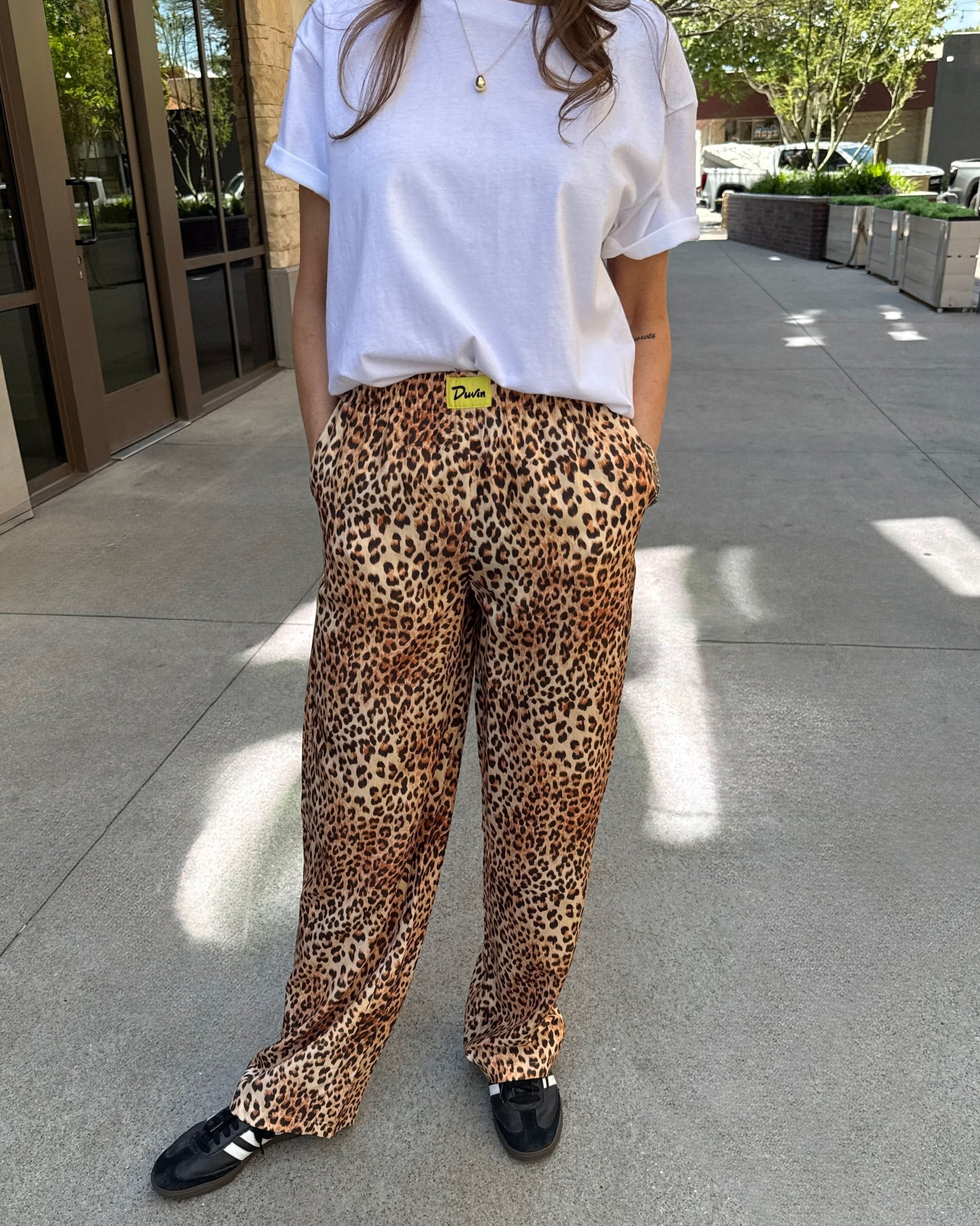 Person wearing a white t-shirt and leopard print pants on a sidewalk.