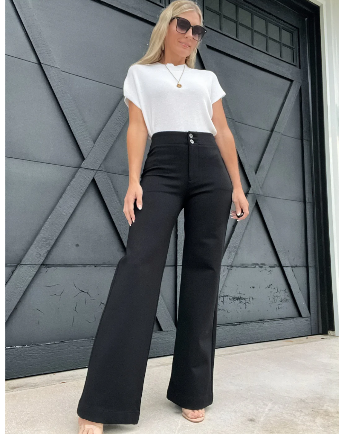 Woman wearing a white top and black high-waisted pants standing in front of a dark gray door.