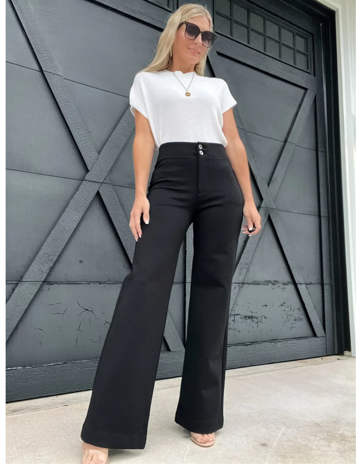Woman wearing a white top and black high-waisted pants standing in front of a dark gray door.