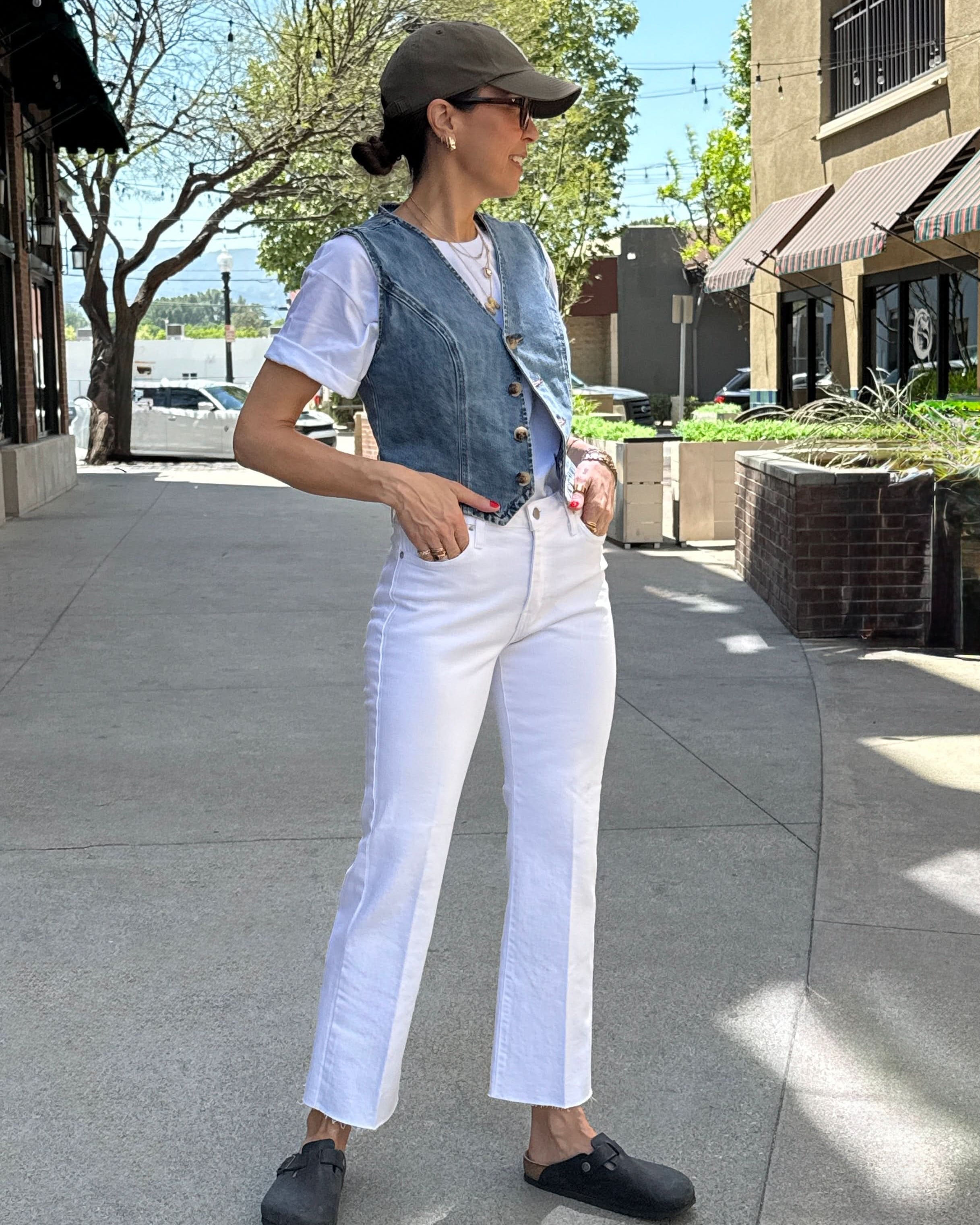 Person wearing a denim vest, white shirt, and white pants on a sidewalk.