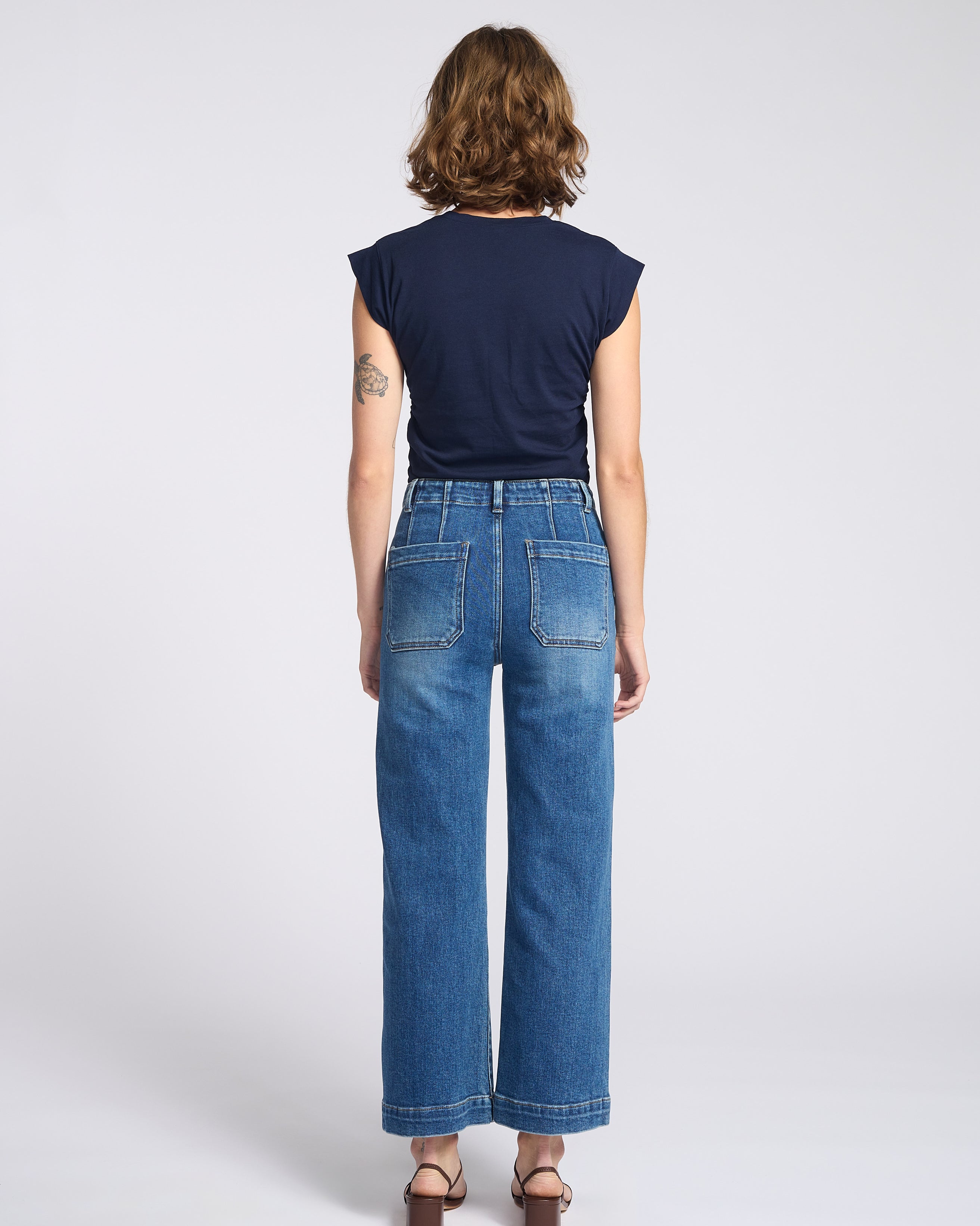 Woman wearing wide legs dark jeans with square back pockets with navy blue shirt