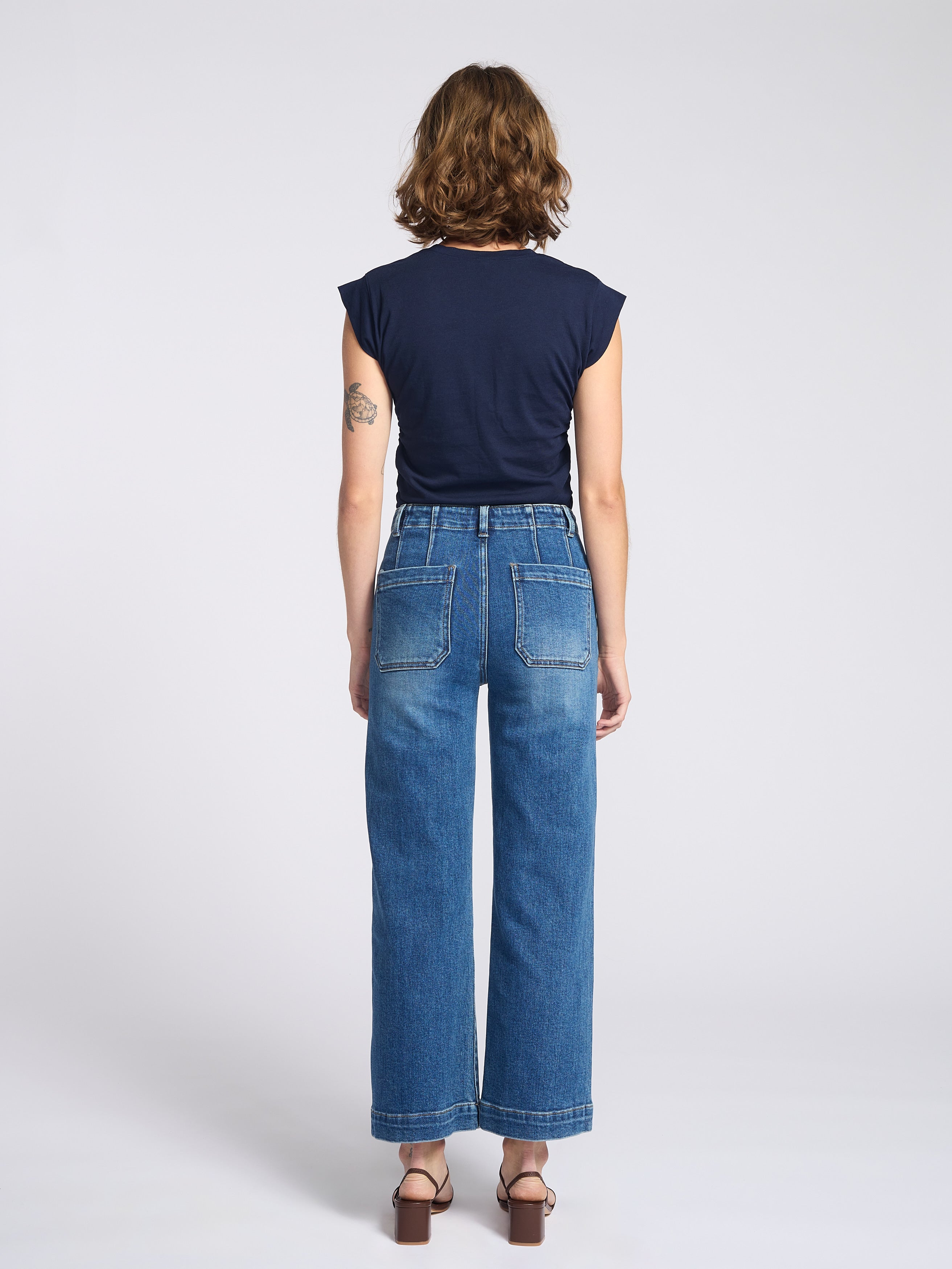 Woman wearing wide legs dark jeans with square back pockets with navy blue shirt