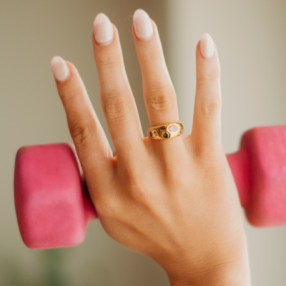 Gold ring with multi shaped and colored gems across the thickest head of the ring