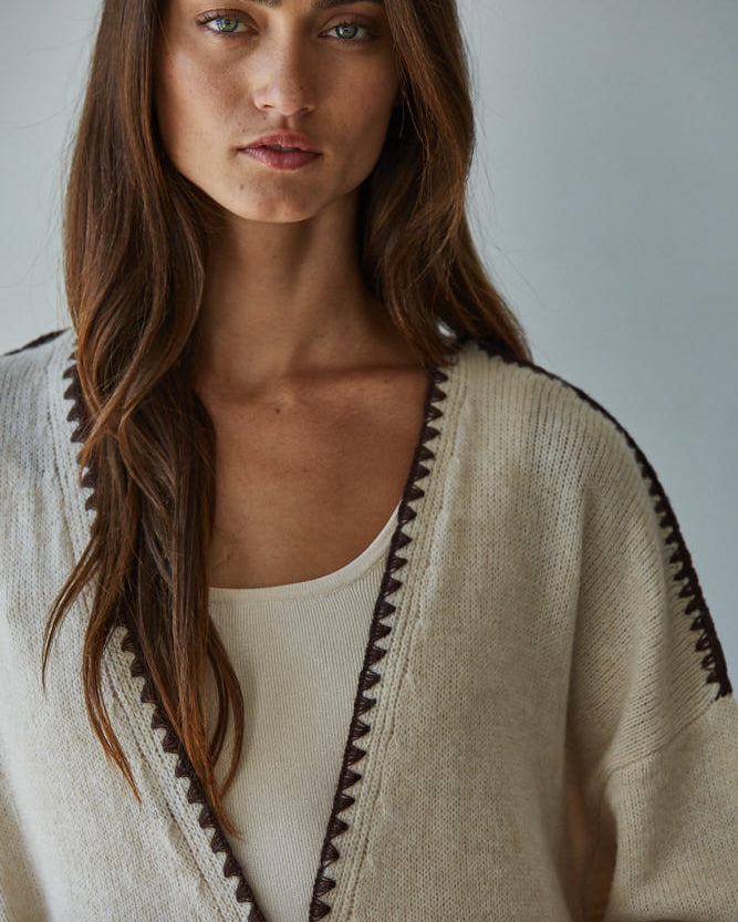 Woman wearing a beige cardigan with black trim against a plain background