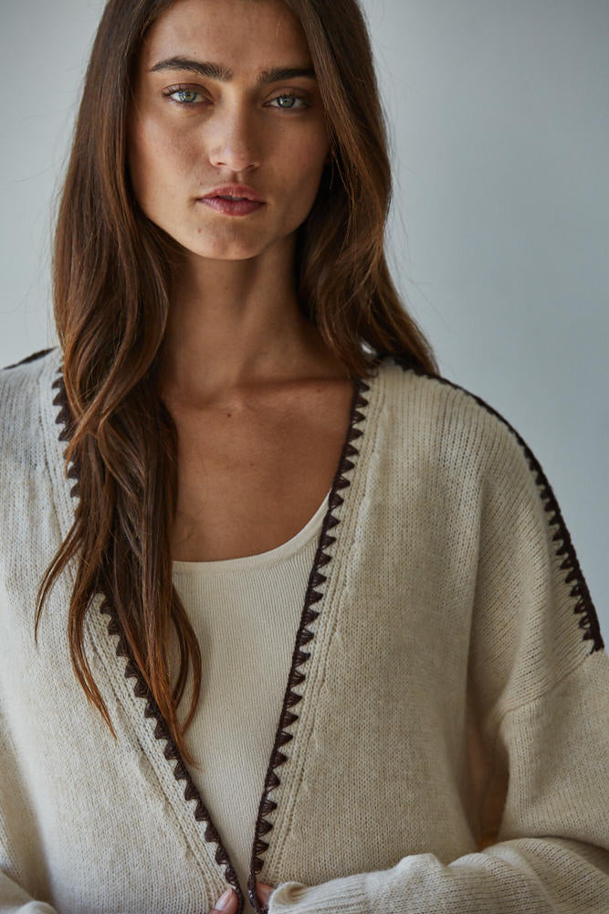 Woman wearing a beige cardigan with black trim against a plain background
