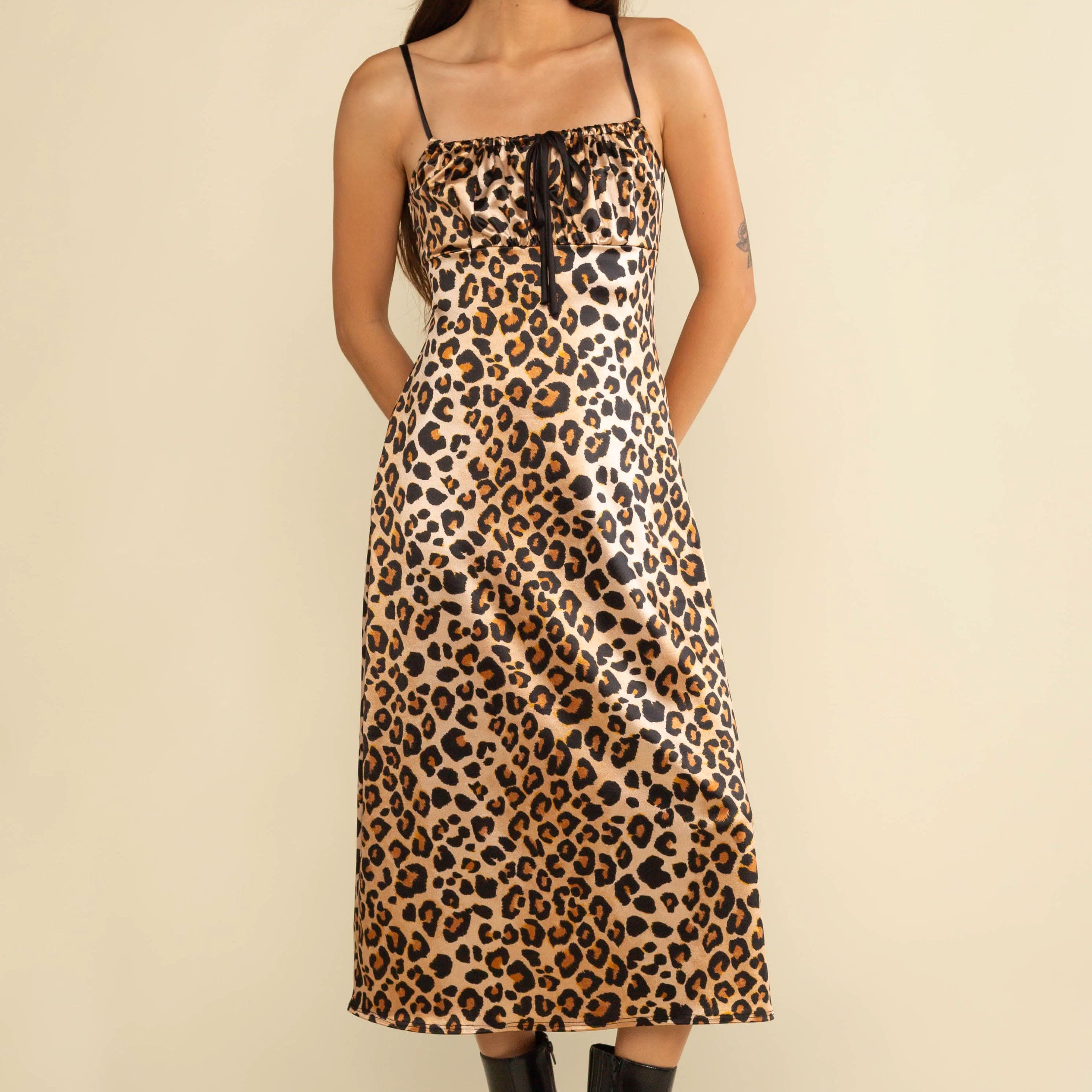 Woman wearing a leopard print dress with black boots on a beige background
