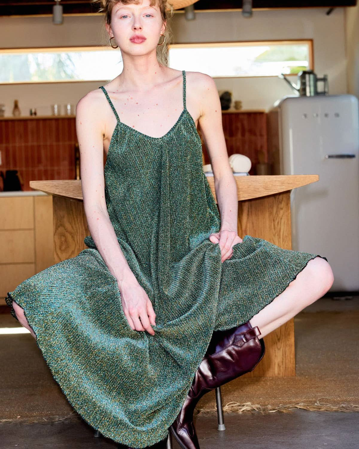 Woman in a green dress sitting on a stool in a casual indoor setting.