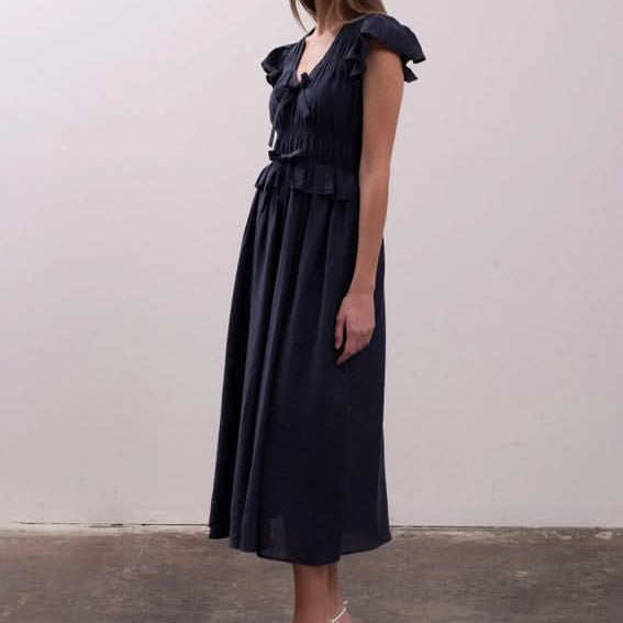 Woman wearing a black dress with ruffled details Moon River Shirred Ruffle Midi Dress