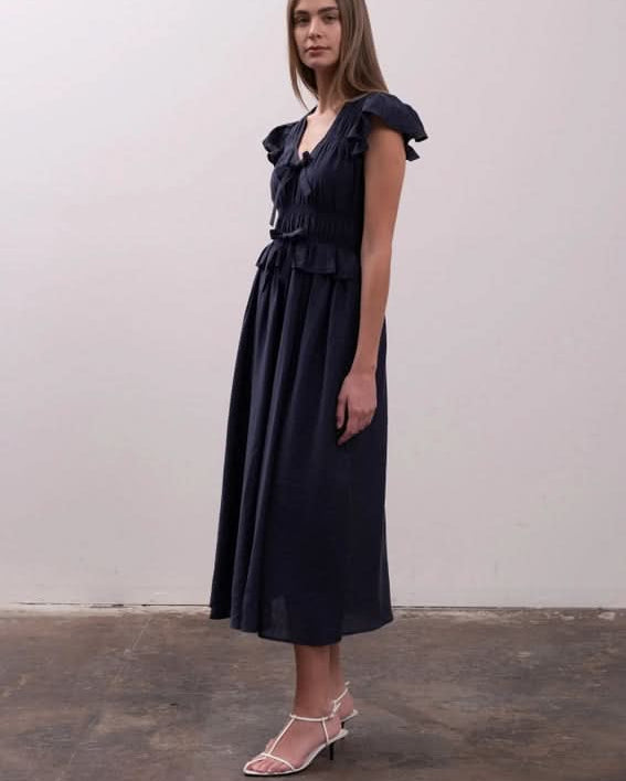 Woman wearing a black dress with ruffled details Moon River Shirred Ruffle Midi Dress