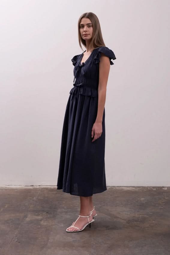 Woman wearing a black dress with ruffled details Moon River Shirred Ruffle Midi Dress