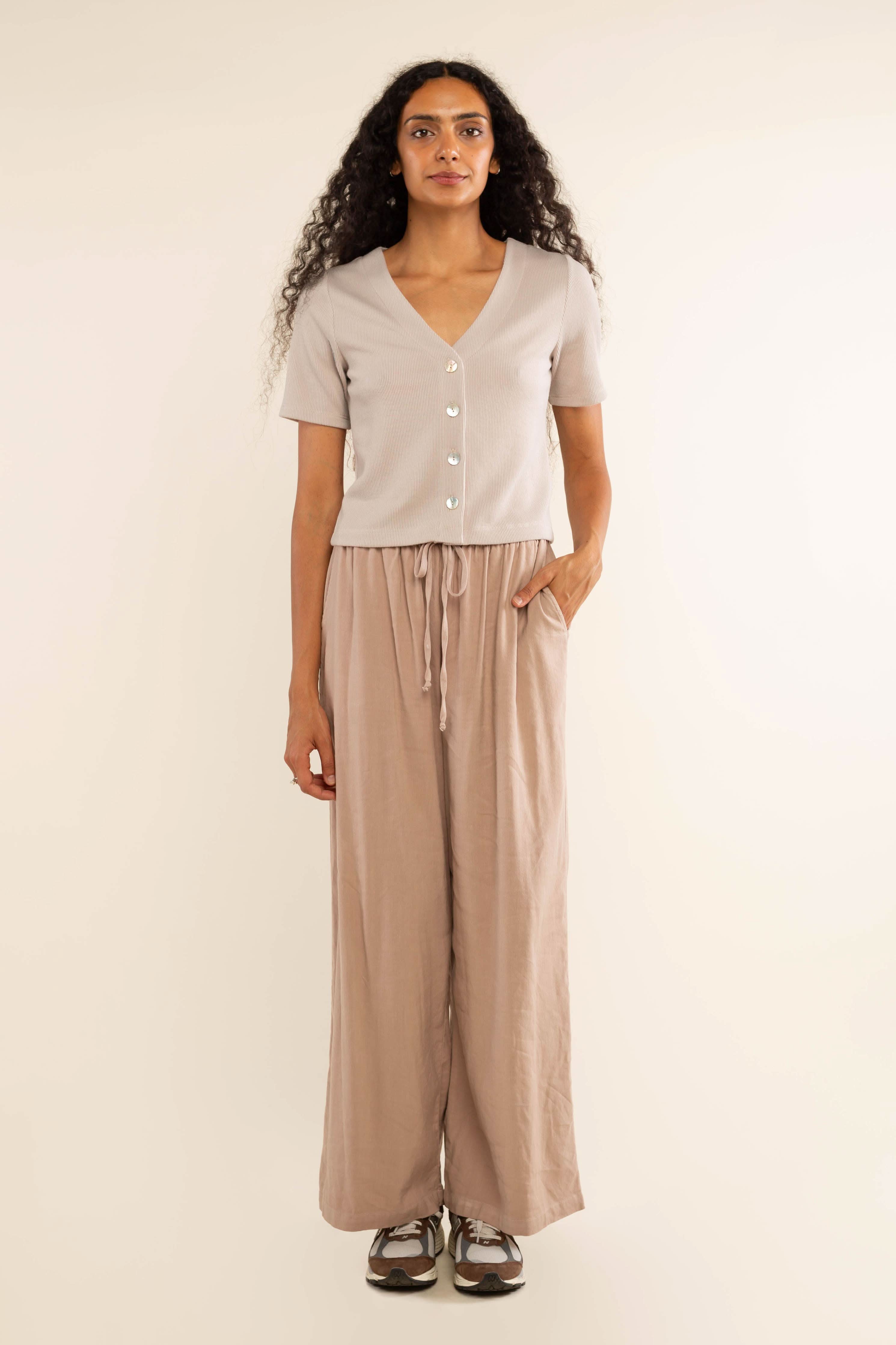 Woman wearing oat colored, ribbed, button down, short sleeve blouse top and beige pants