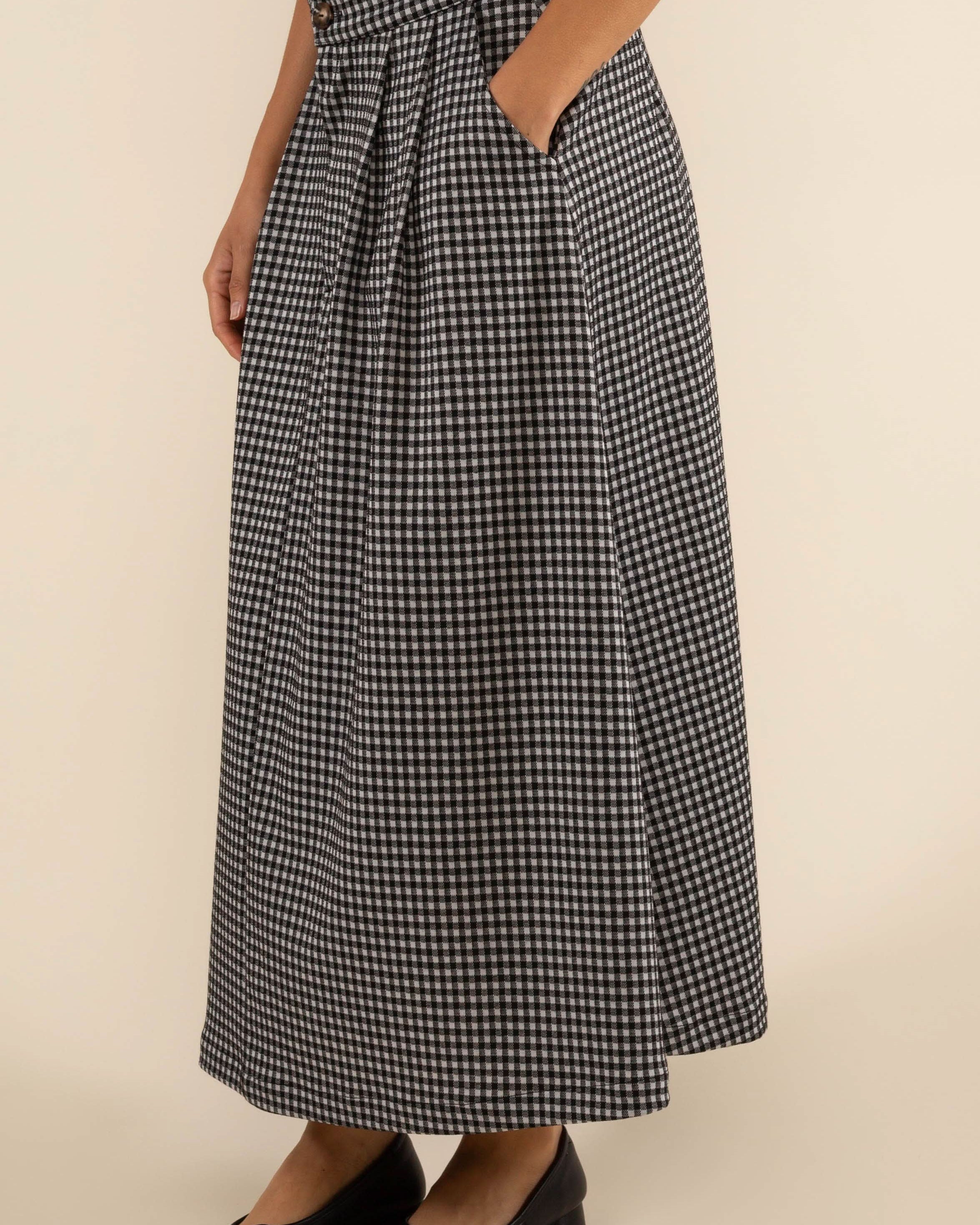 Person wearing checkered skirt with pleats at the front and side pockets.