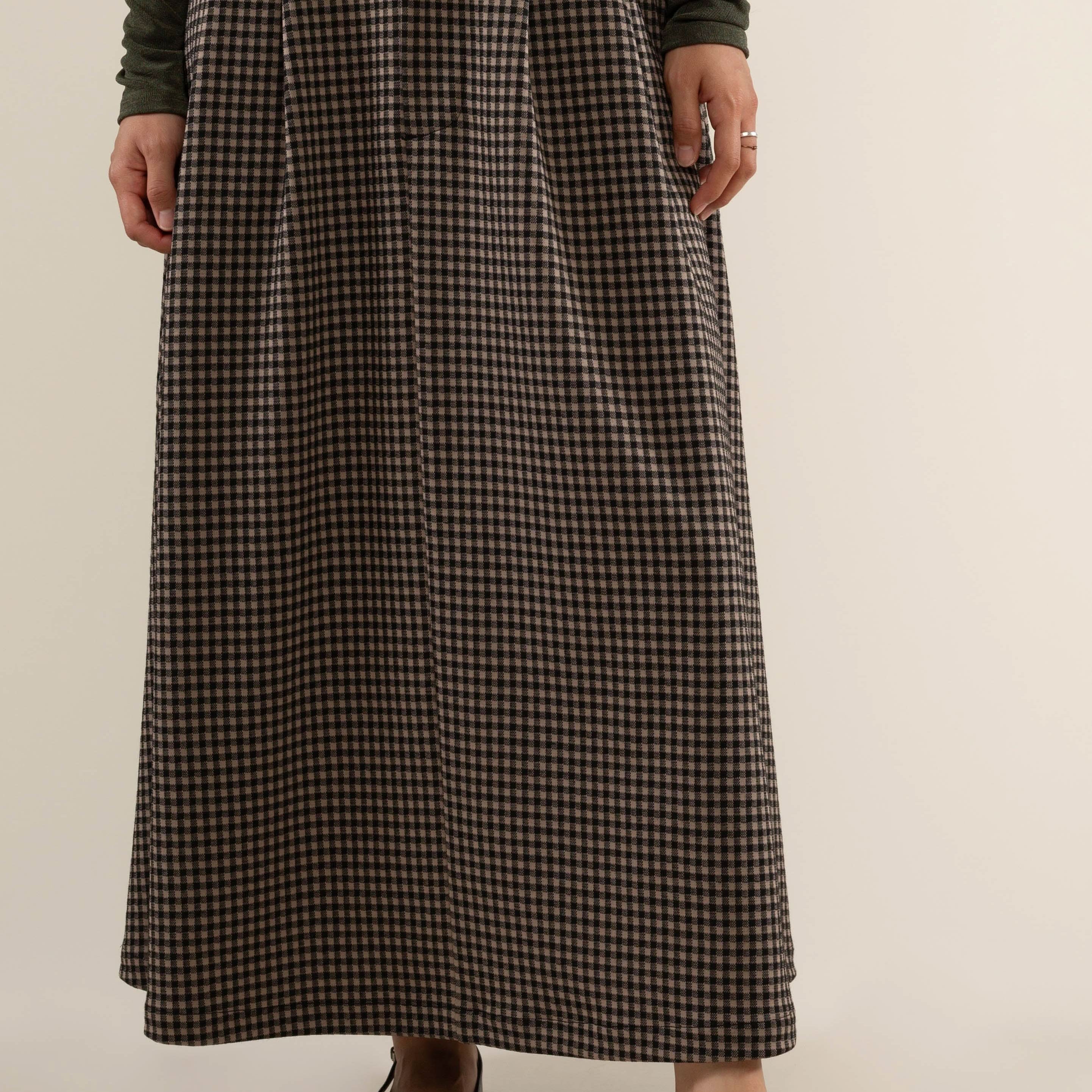 Person wearing a long plaid skirt with pleats at the front and side pockets.