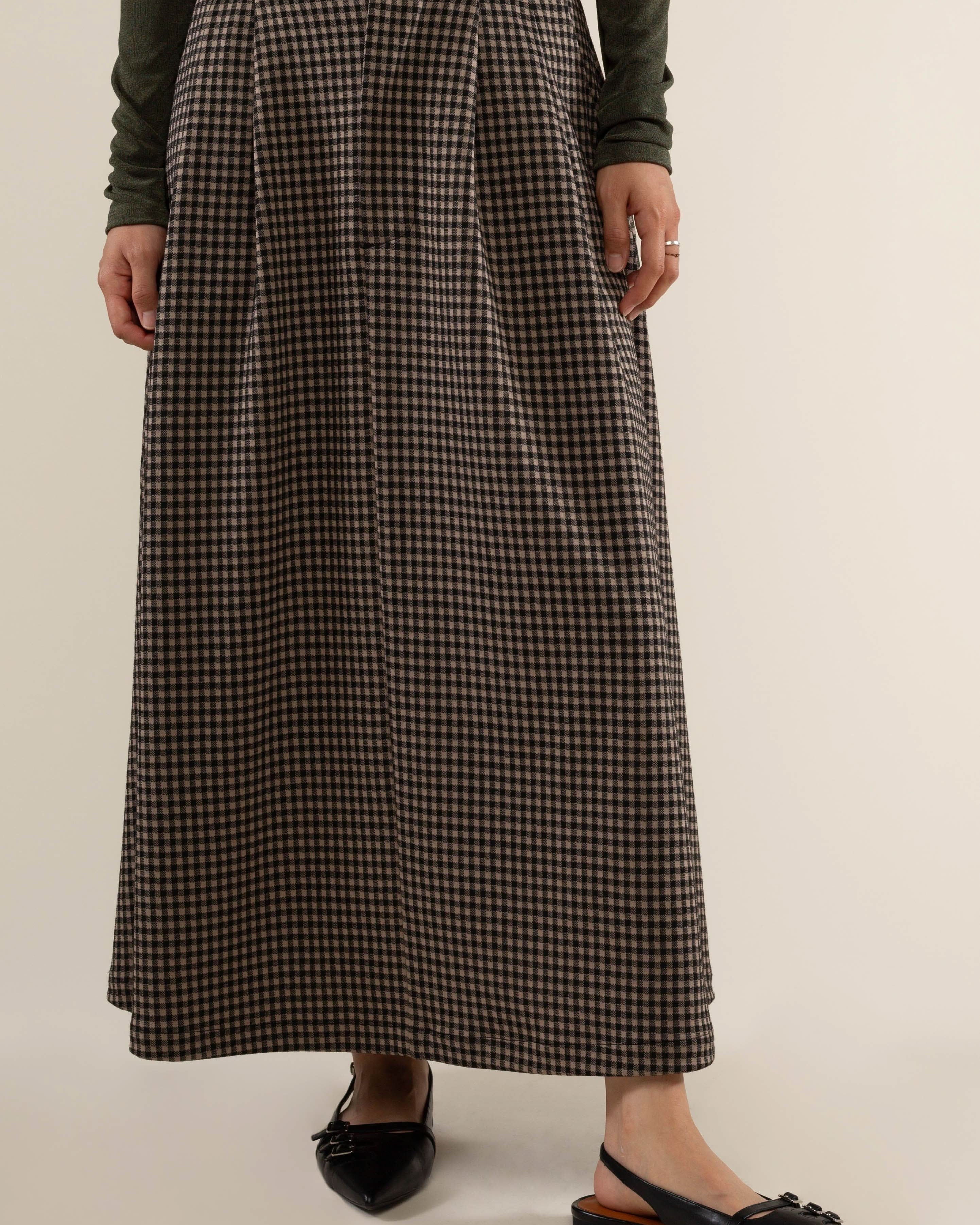 Person wearing a long plaid skirt with pleats at the front and side pockets.