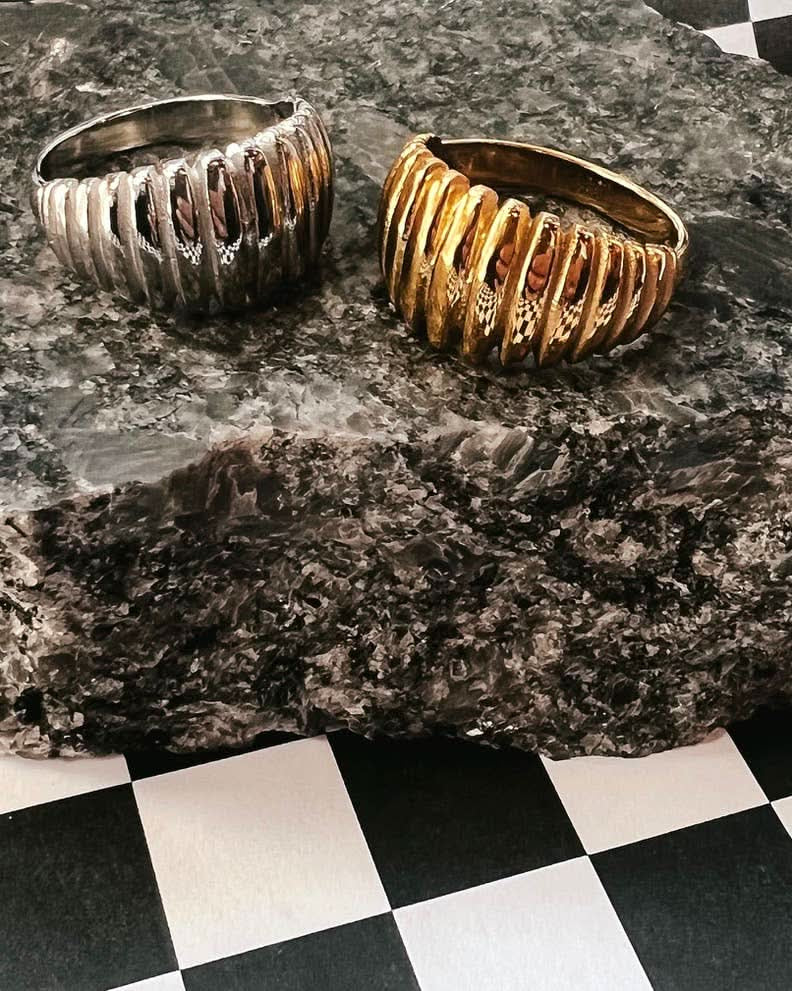 Two ribbed metal cuffs, one silver and one gold, on a textured surface.