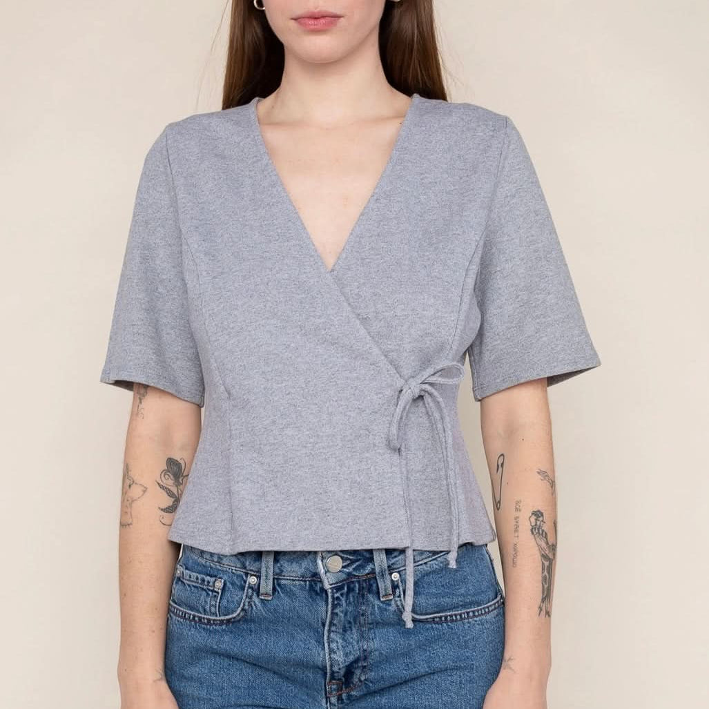 Woman wearing a grey wrap short sleeve shirt with blue jeans