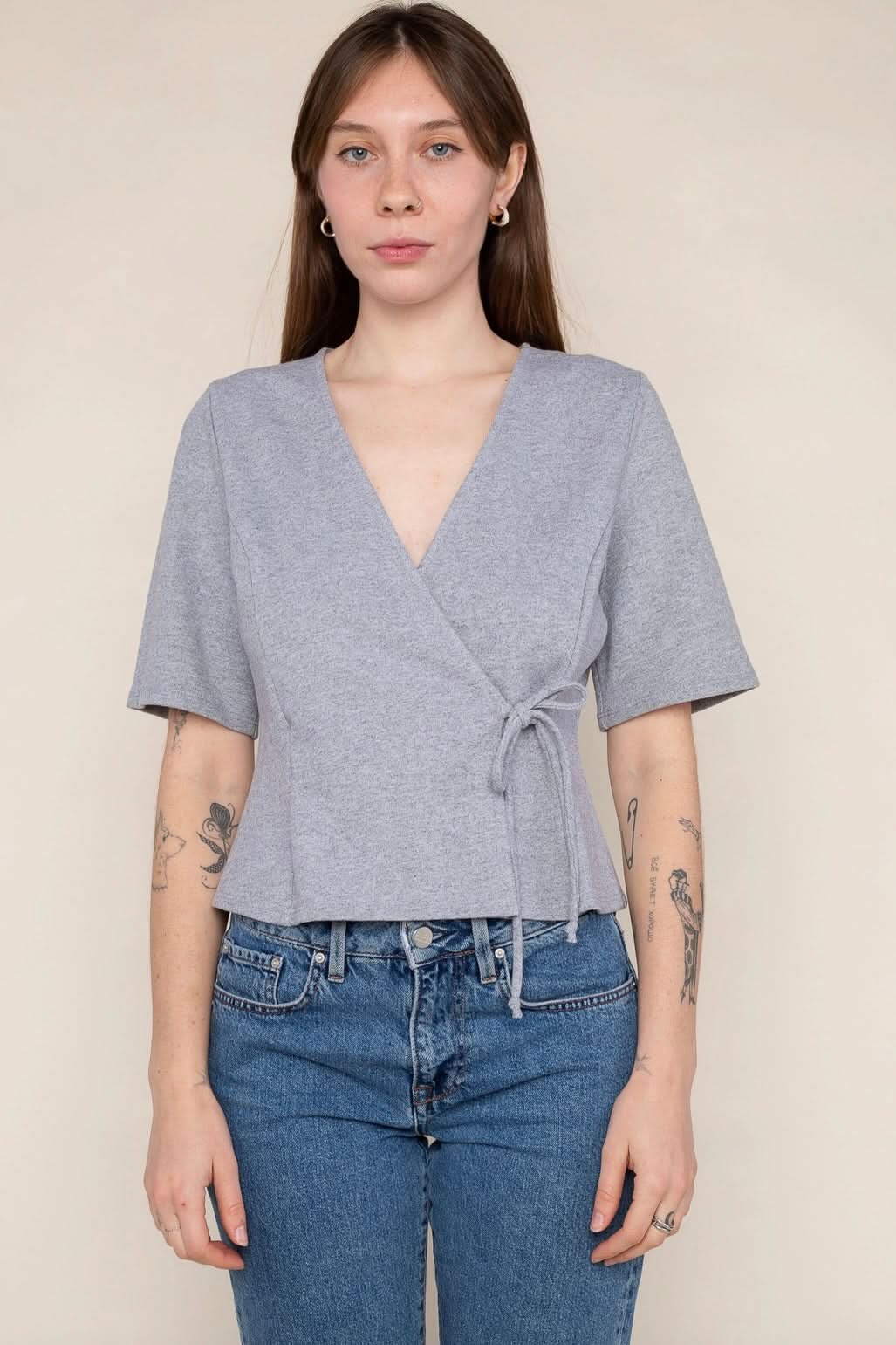 Woman wearing a grey wrap short sleeve shirt with blue jeans