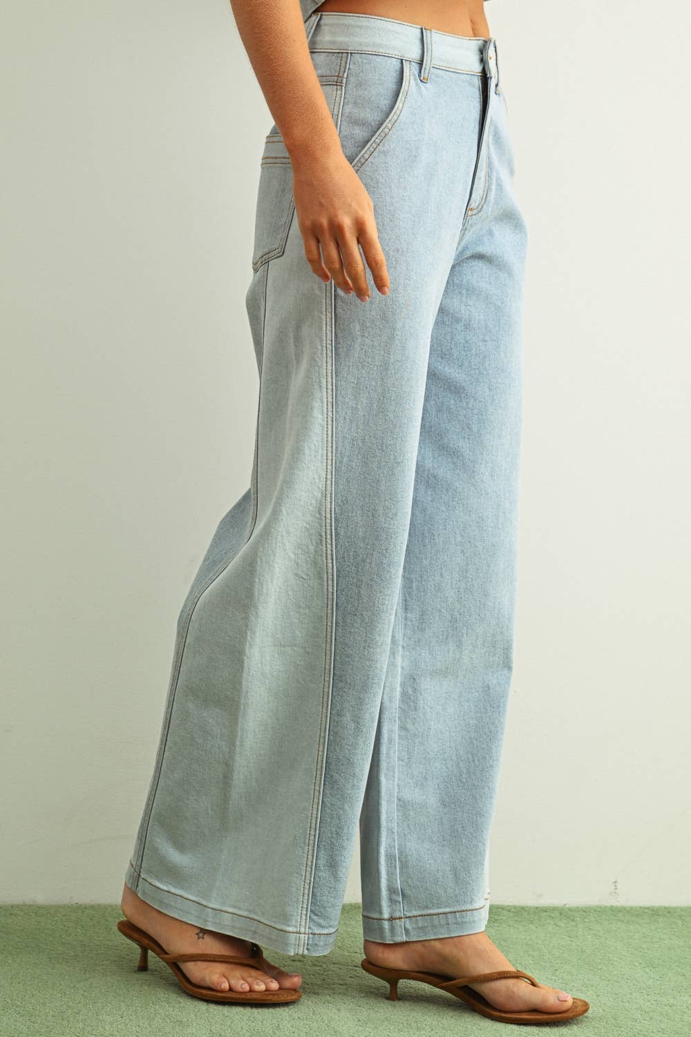 Woman wearing light denim jeans and light brown shoes standing behind a white background