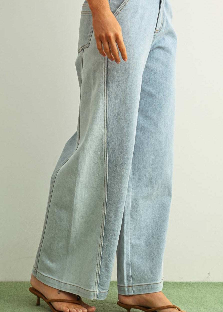 Woman wearing light denim jeans and light brown shoes standing behind a white background