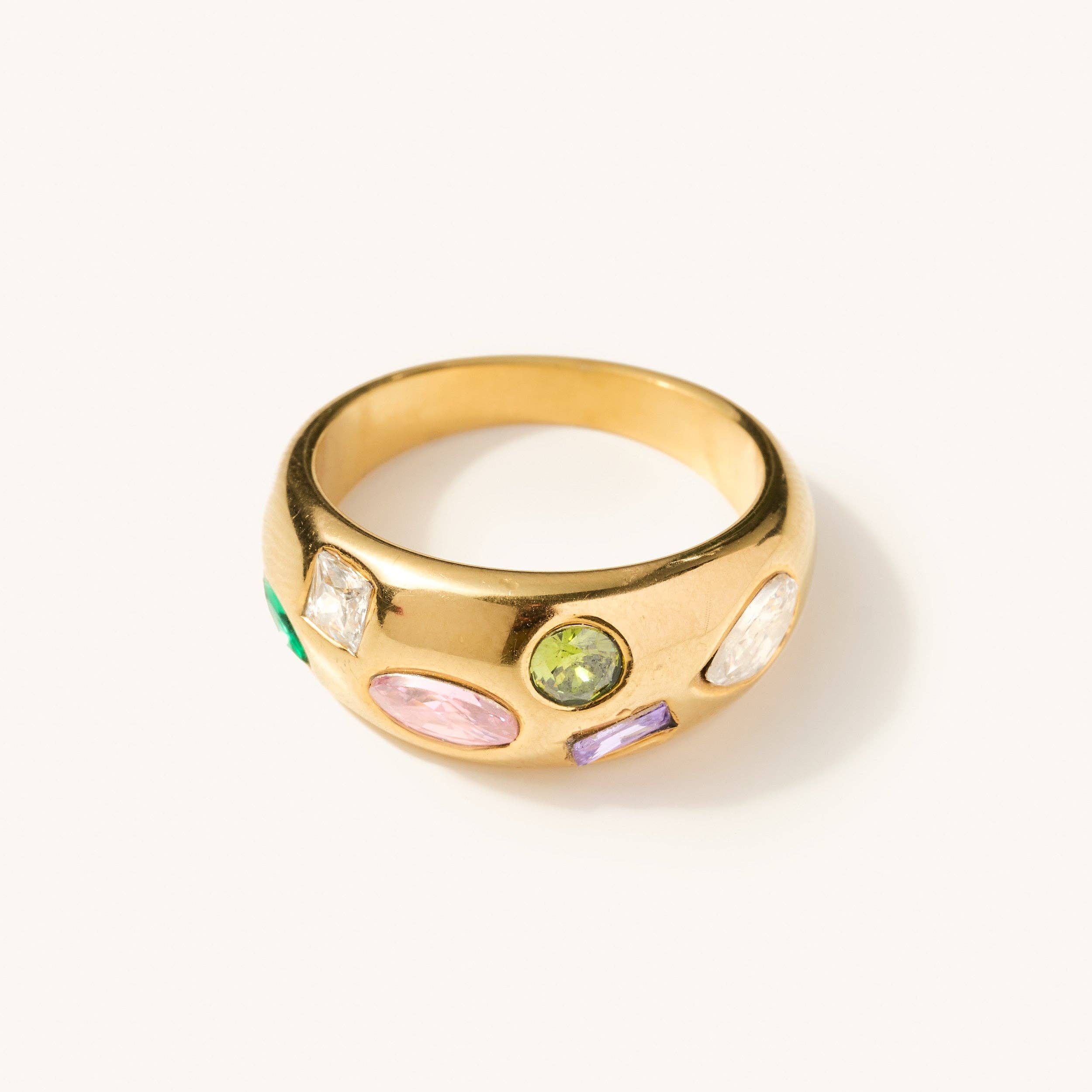 Gold ring with multi shaped and colored gems across the thickest head of the ring 