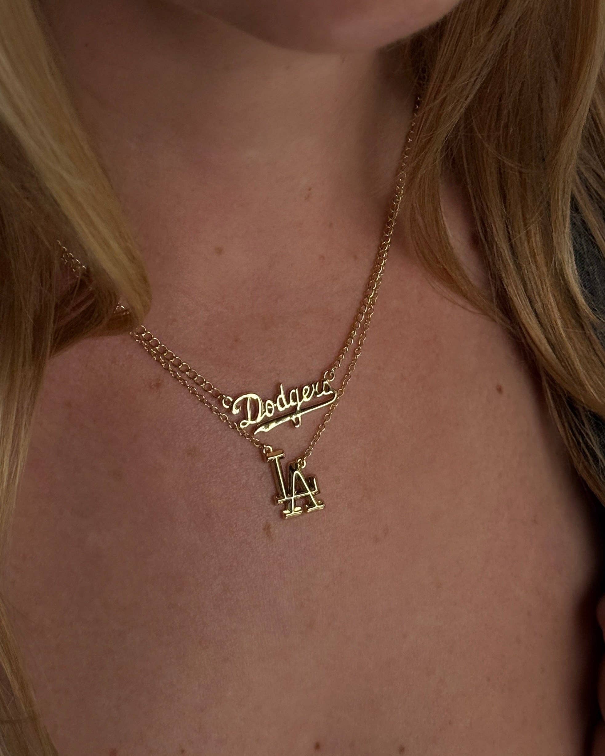 Gold necklace with 'Dodgers' and 'LA' charms on a person's neck.