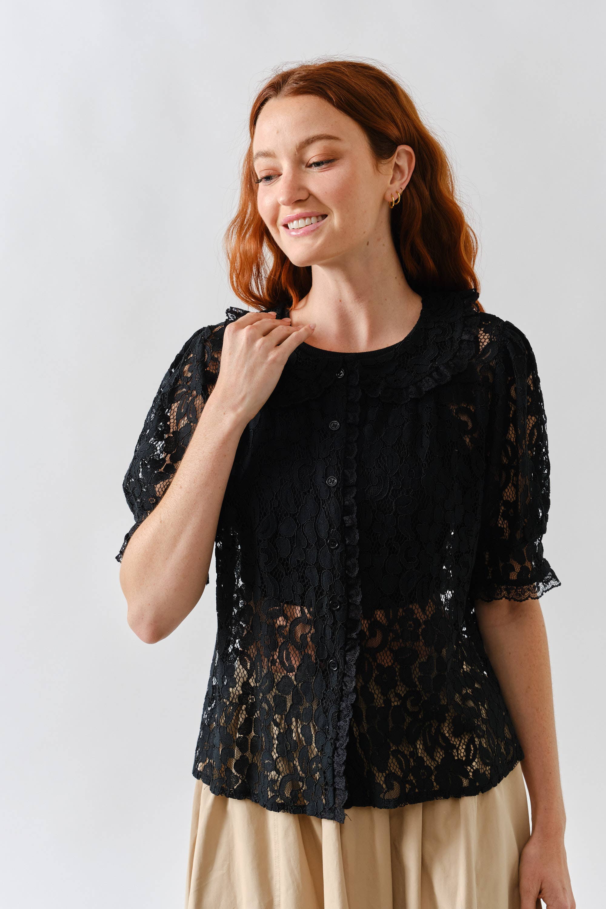 Woman wearing black lace button up blouse with beige bottoms 