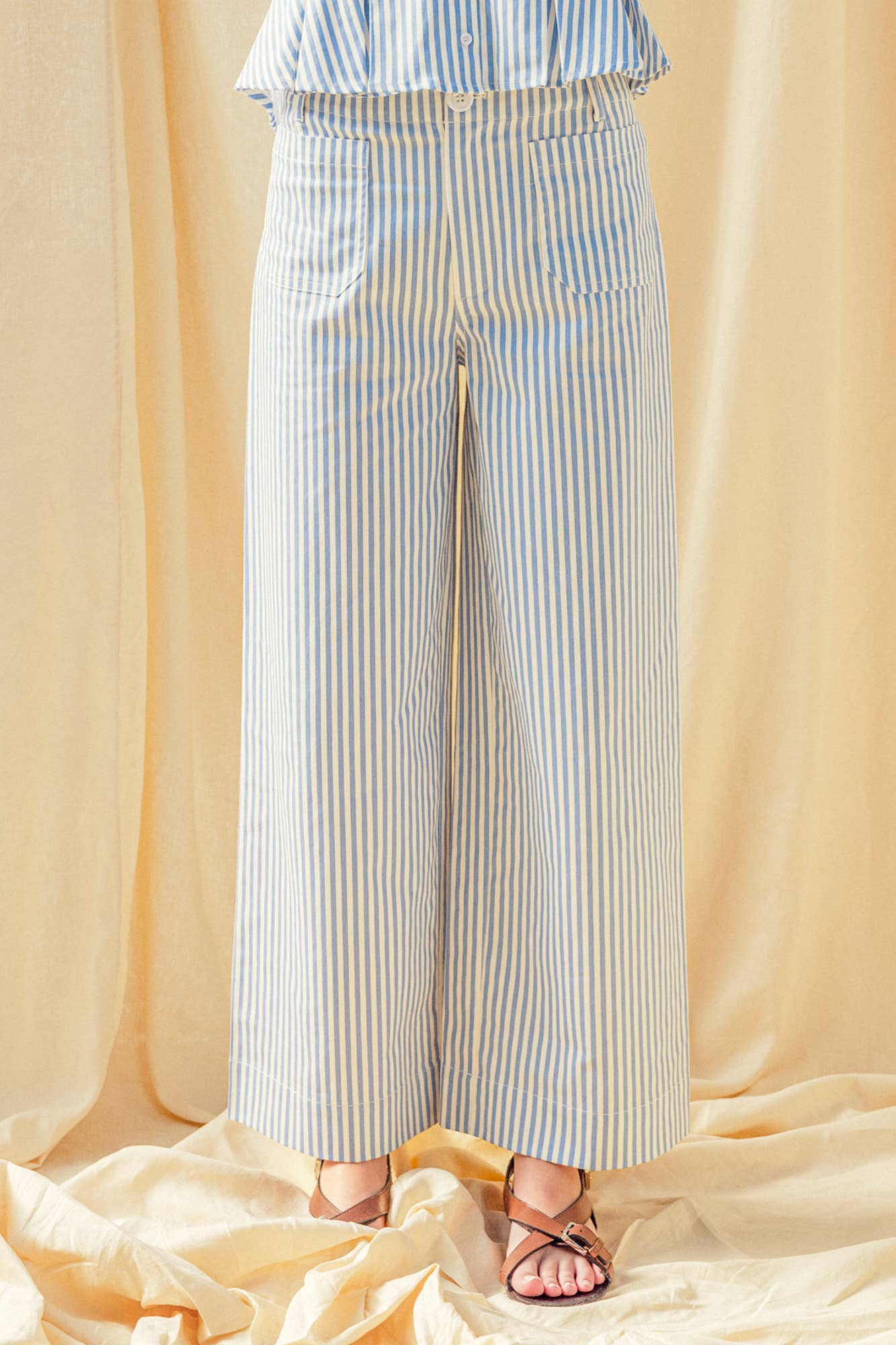 Person wearing a blue and white striped outfit with wide-leg pants on a beige background